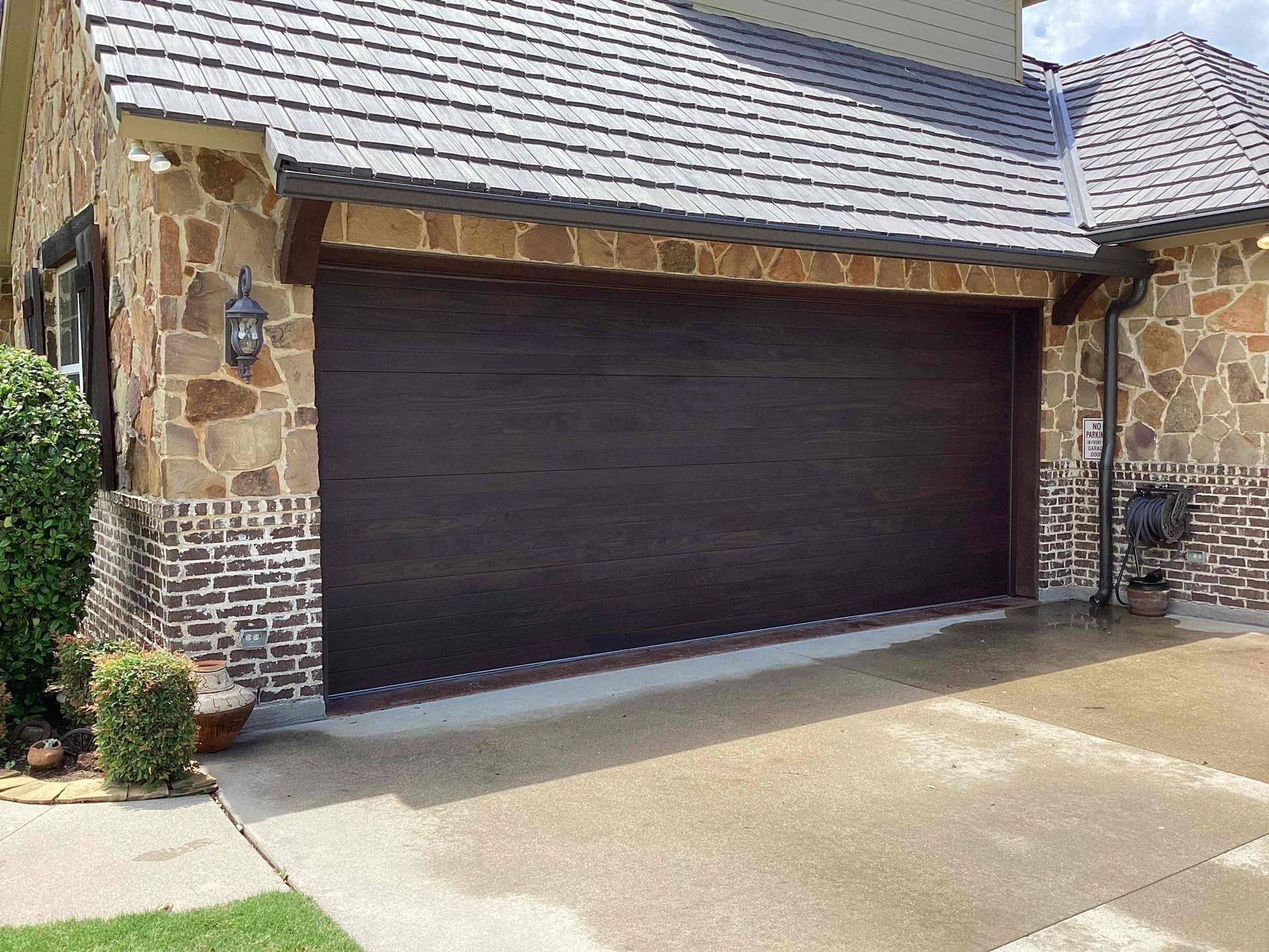 A dark brown horizontal panel garage door on a house with stone and brick exterior walls and a gray tiled roof.