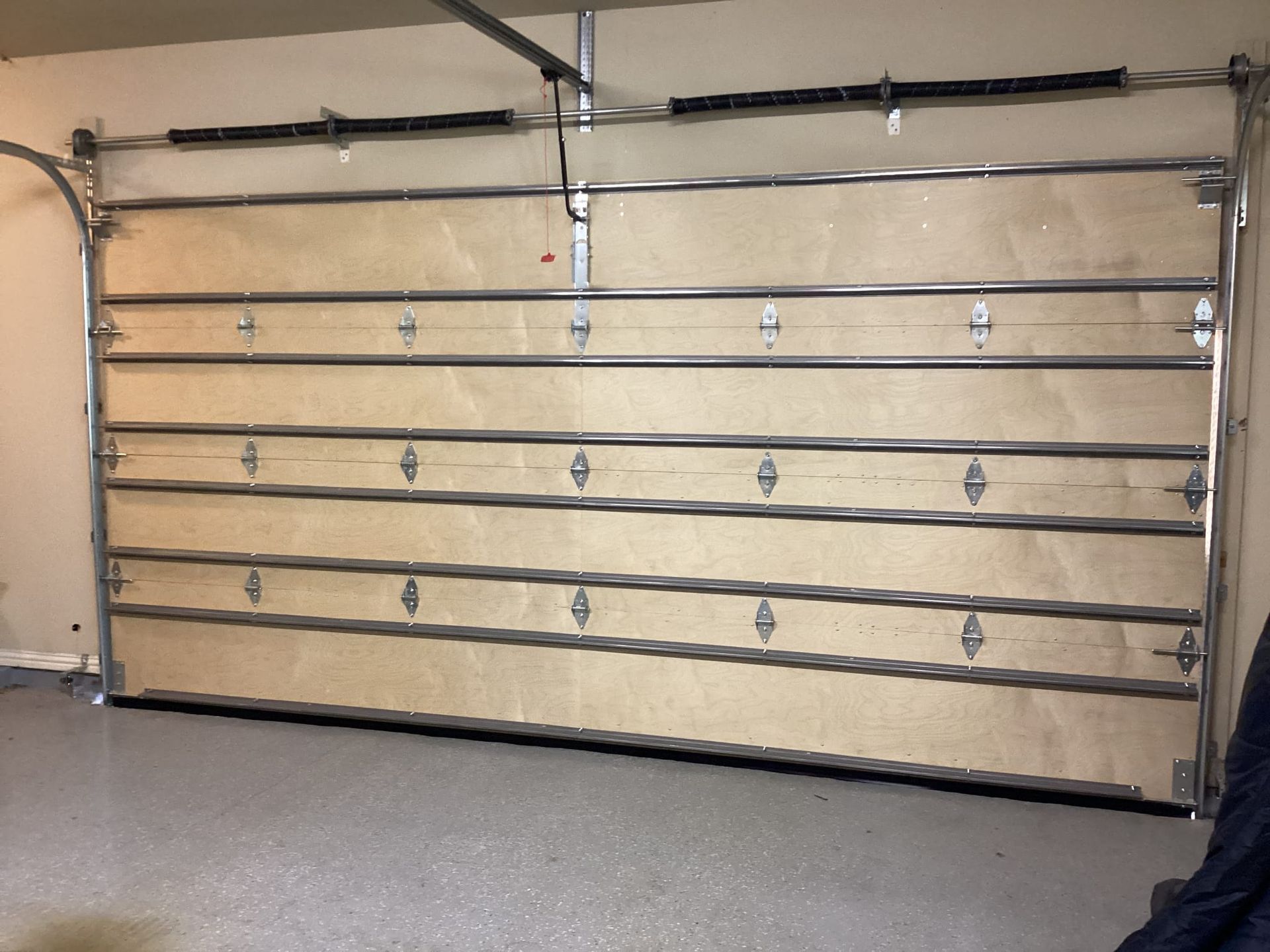 A closed sectional garage door inside a garage, featuring light wood panels, silver metal tracks, and hardware.