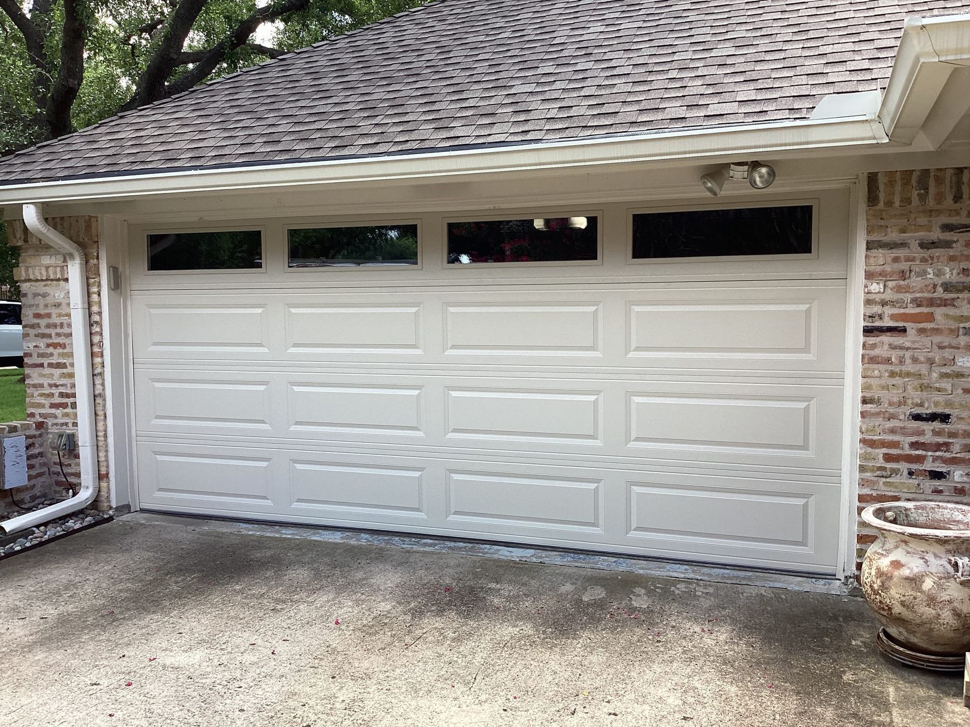 A white, four-panel residential garage door with top-row rectangular windows, set into a brick exterior wall.