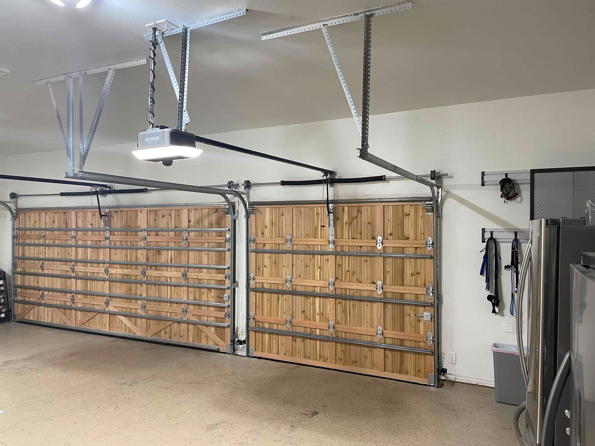 Two wooden garage doors with metal frames and ceiling-mounted openers in a clean, spacious residential garage.