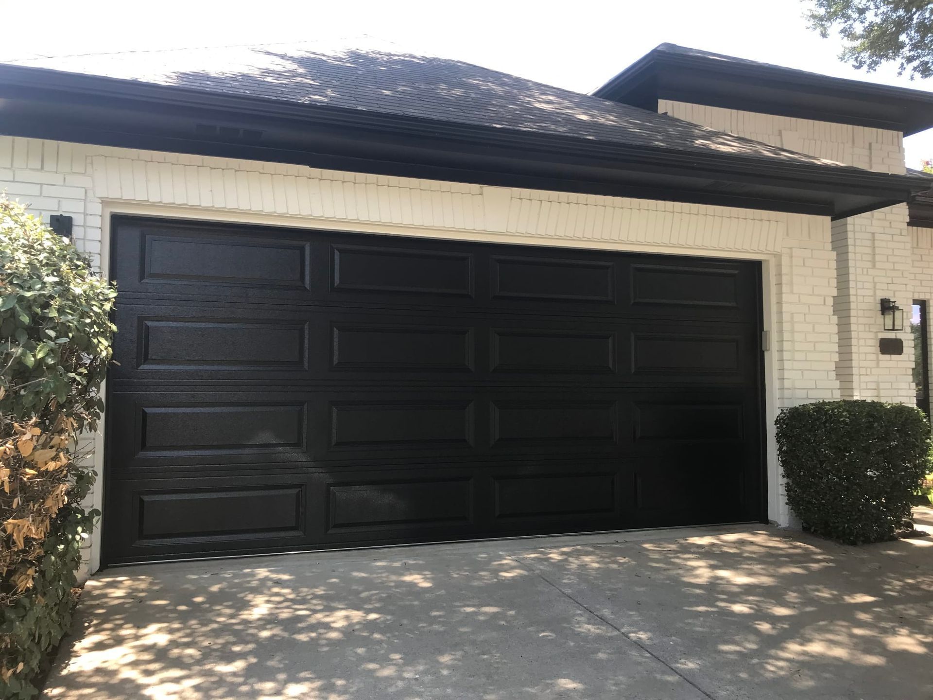 A modern garage with a black multi-panel door set into a white brick exterior wall, viewed from a driveway.