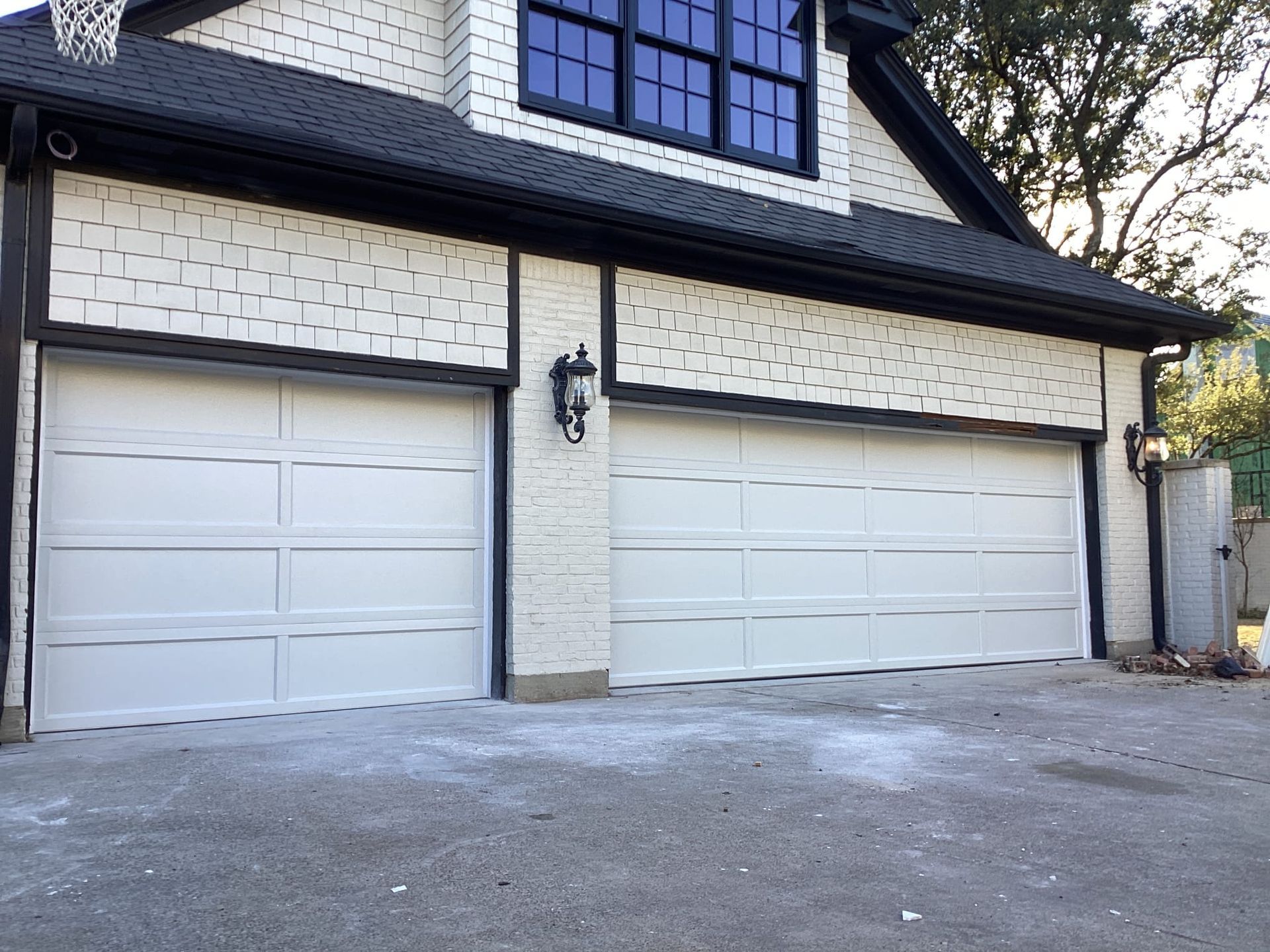 A modern two-car garage with white paneled doors, black trim, and white textured brick siding.