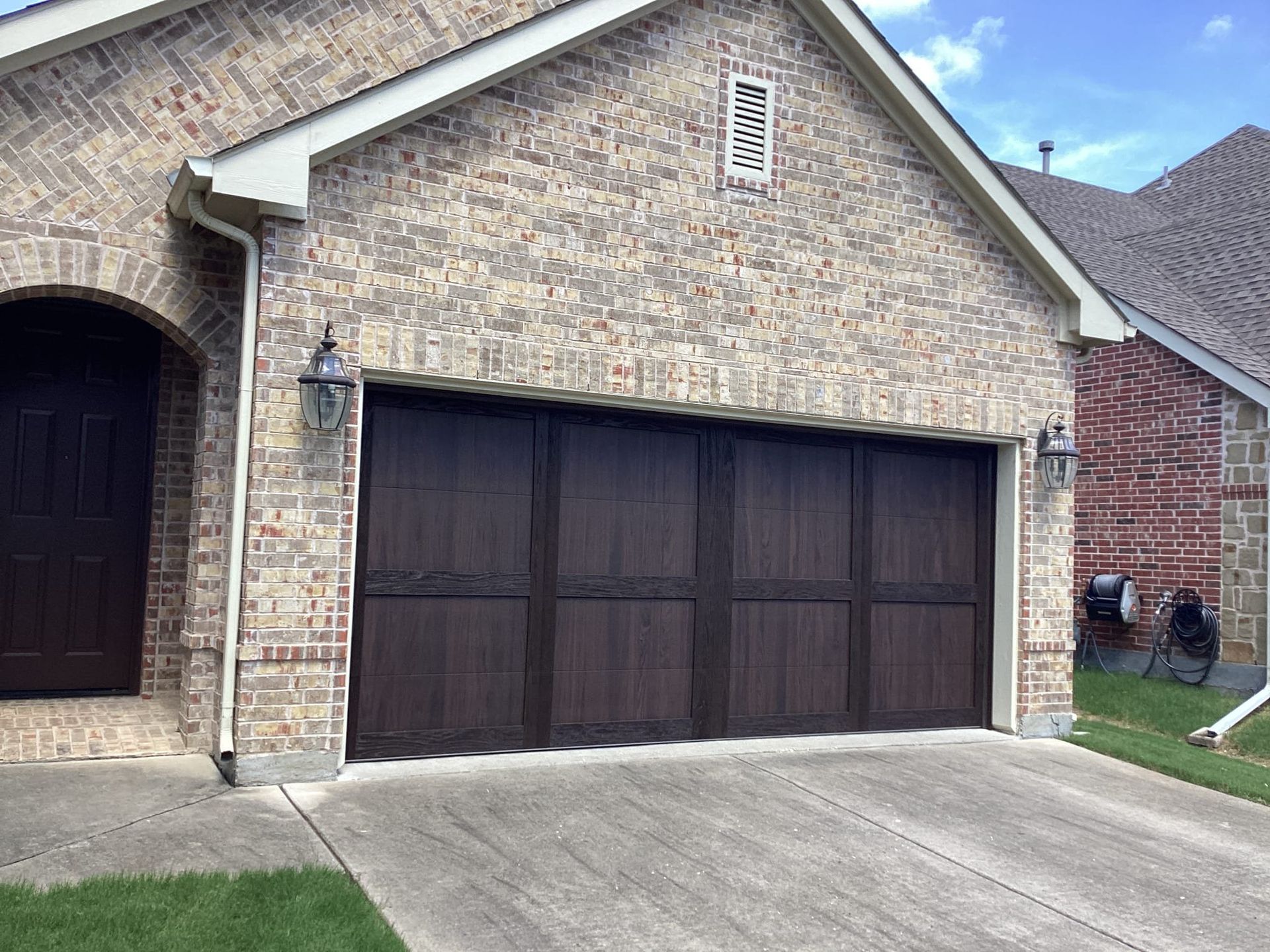 Garage with brown wooden door, brick exterior, and concrete driveway.
