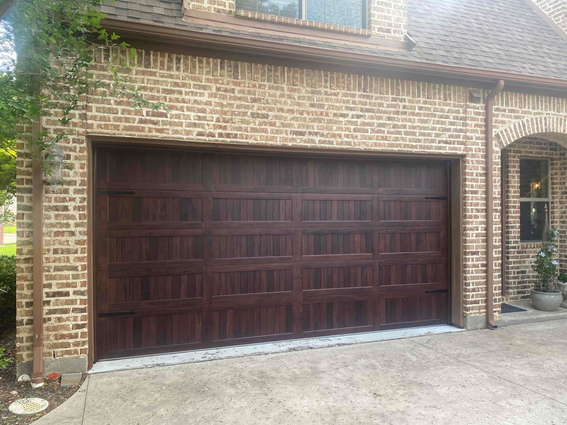 A dark-brown, paneled wooden garage door on a tan brick house with a concrete driveway.