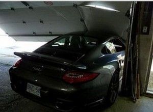 Dark Porsche Turbo wedged in a garage doorway, partially crushing the door.