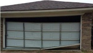 Damaged white garage door, partially open and bent, attached to a brick building.