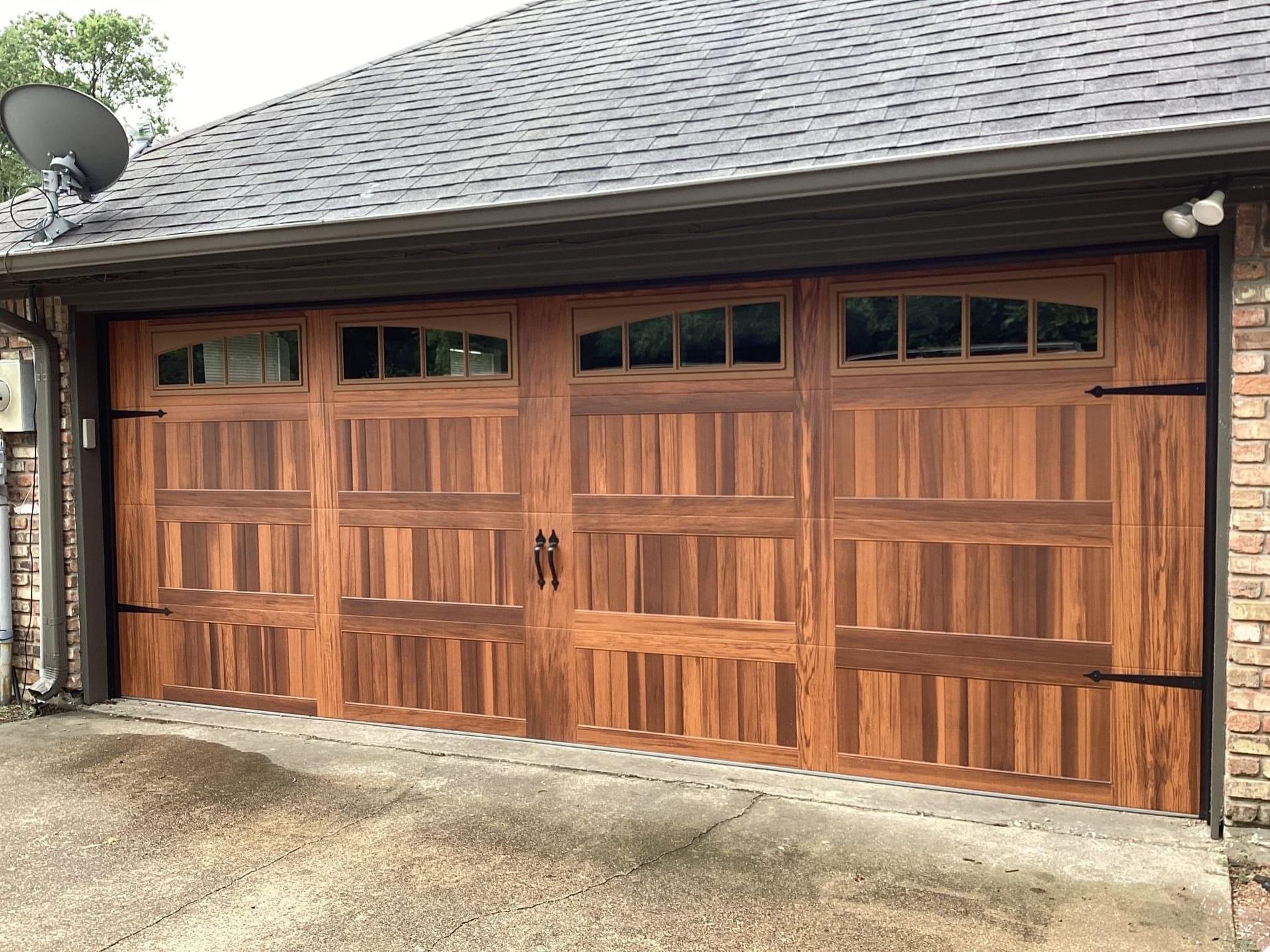 A two-car garage with wood-grain doors, each featuring four upper window panes and black decorative hardware.