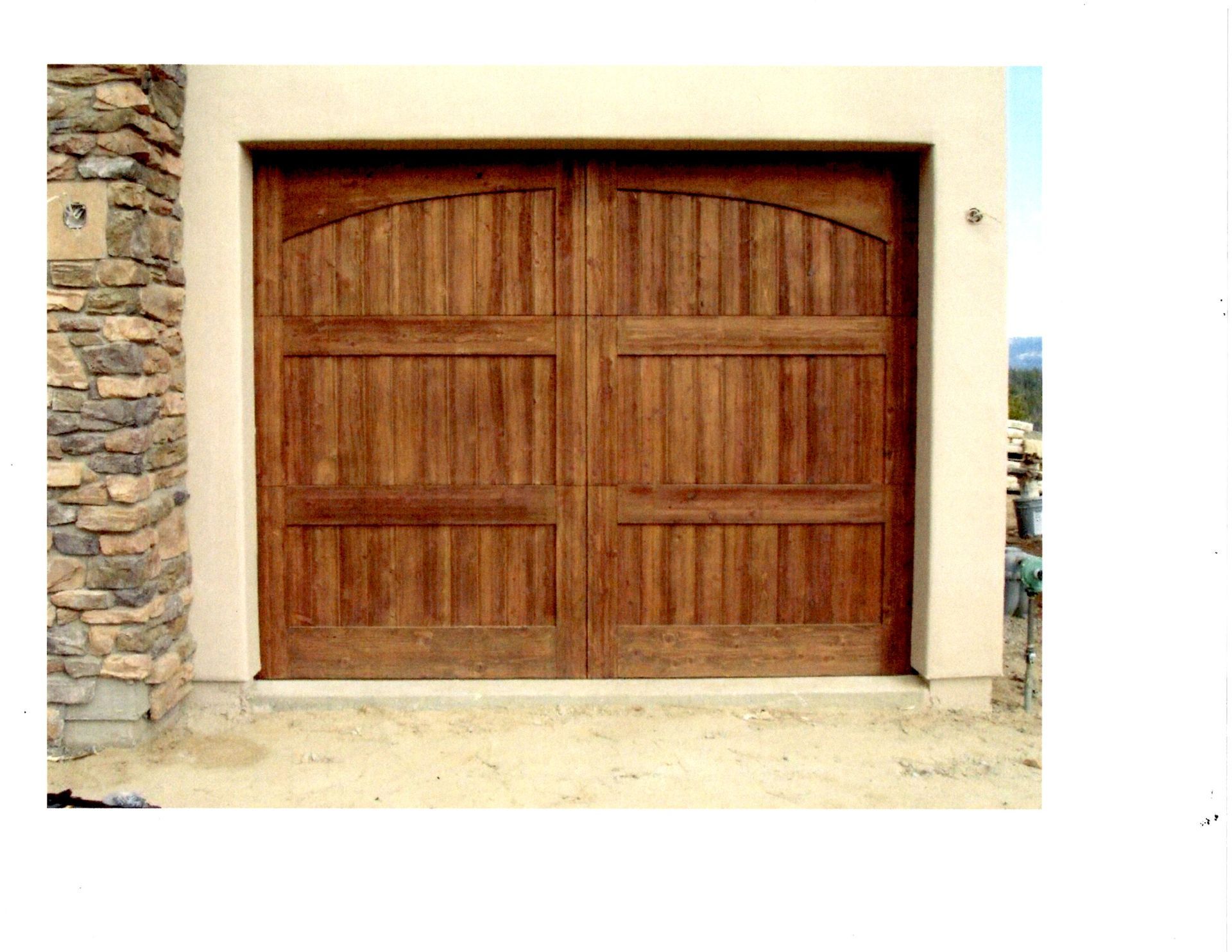 A wooden carriage-style garage door with vertical paneling, set in a light stucco wall next to stone masonry.