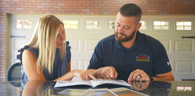 A man and woman looking at a book together at a table. They are both pointing at the pages. Garage in the background.