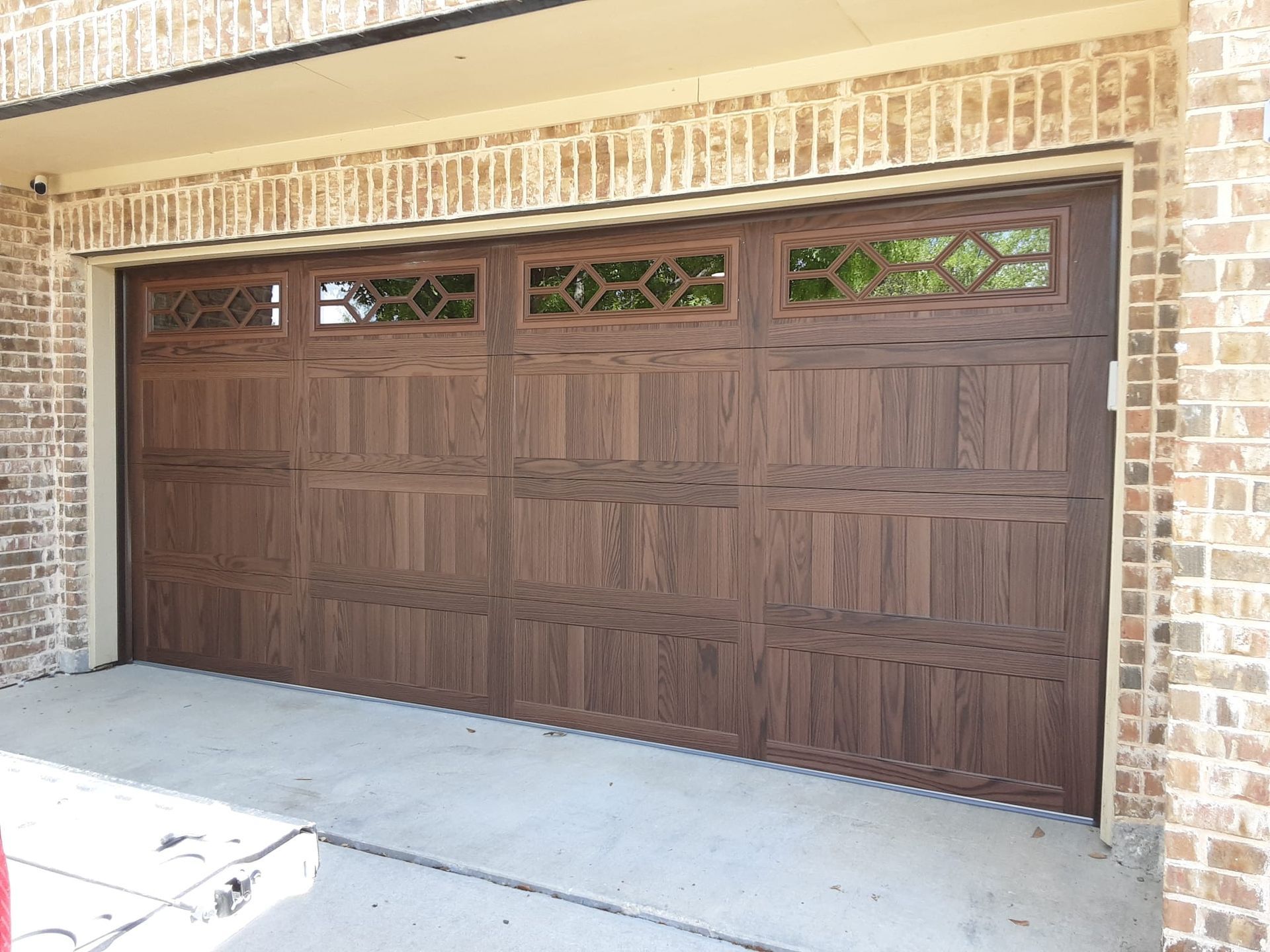 A dark wood-toned garage door with recessed panels and a row of windows with diamond-patterned inserts, set in brick.