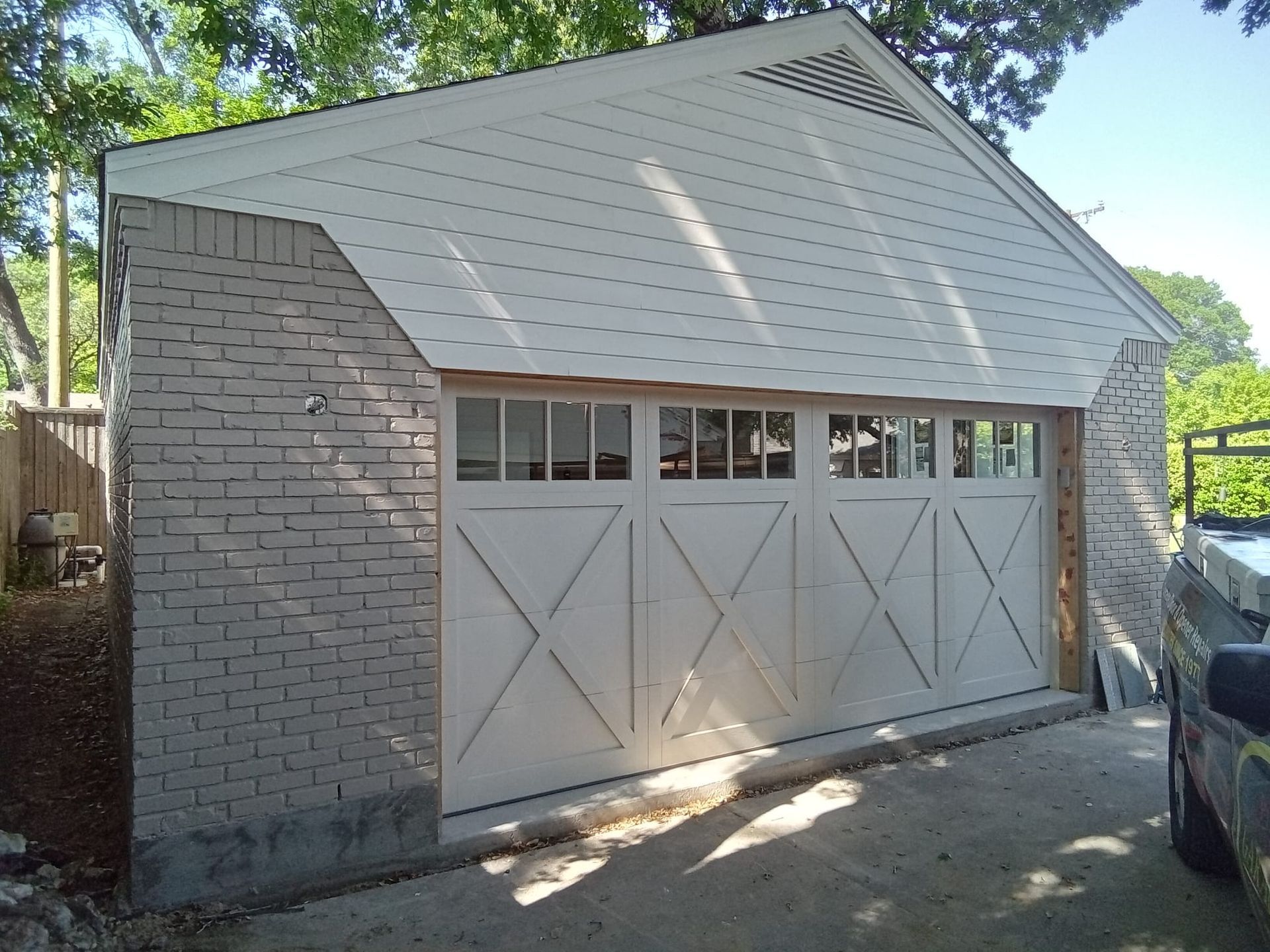 A detached garage with light-colored brick exterior, white wood-paneled siding, and a four-section white garage door.