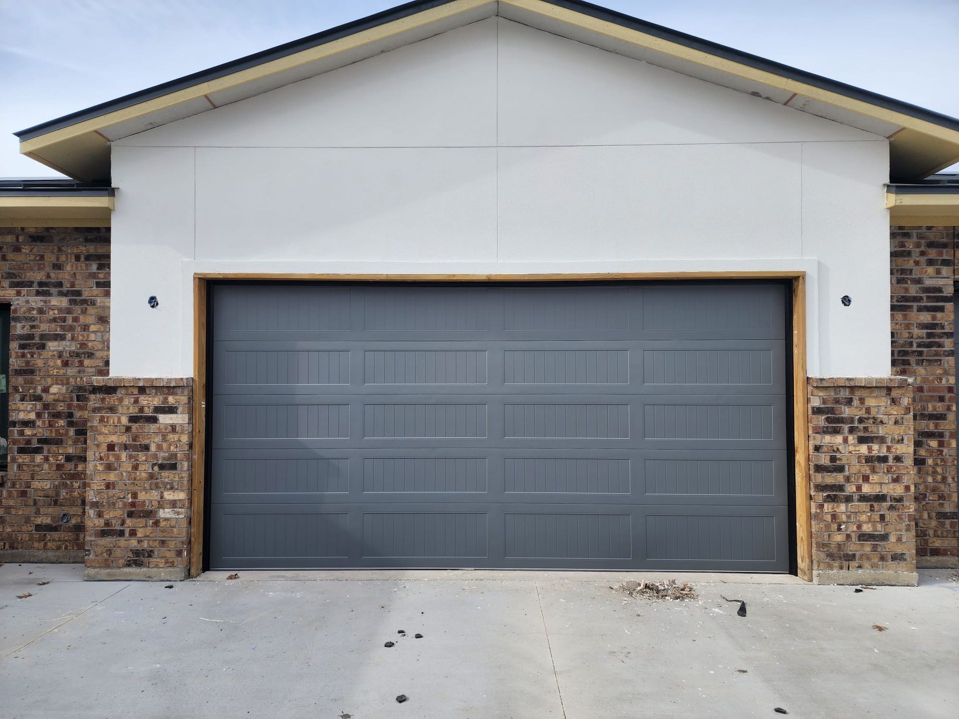 A grey garage door on a house with a white gable and brick siding.
