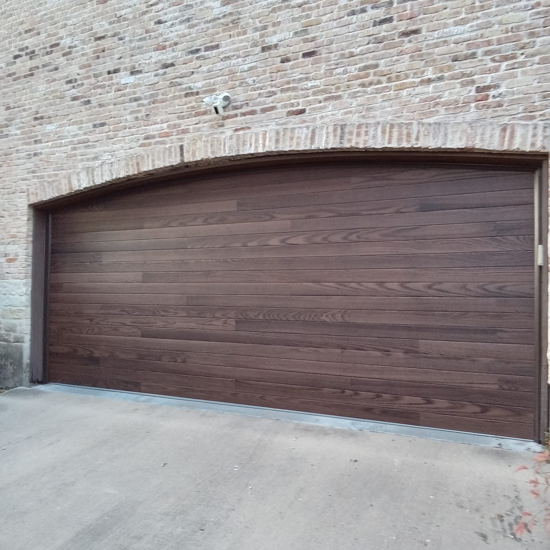 A dark brown horizontal-plank garage door set into an arched brick wall.