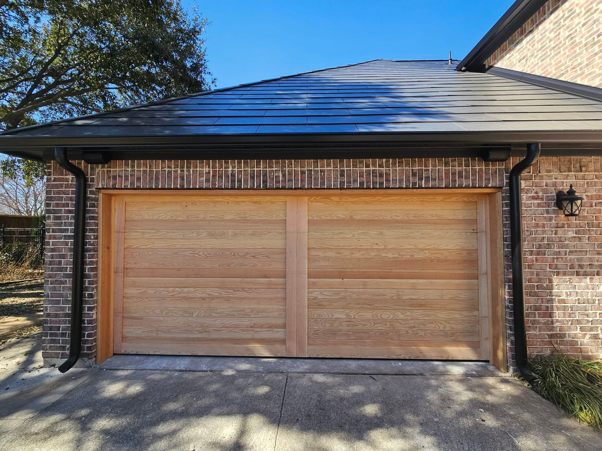 A wooden two-car garage door with a horizontal panel design centered in a brick exterior wall under a dark metal roof.
