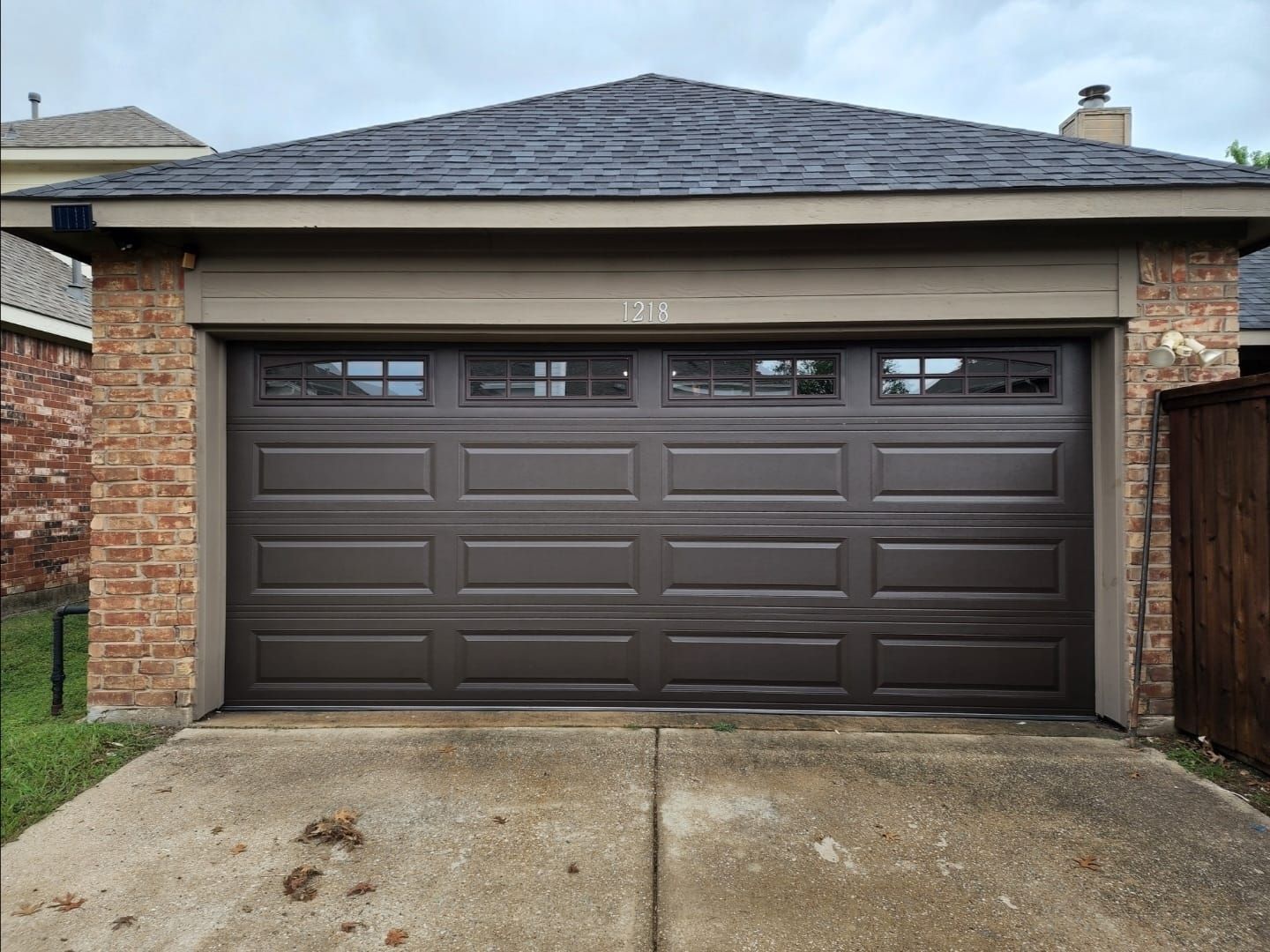 A brown garage door with rectangular panels and a top row of small, square windows, set in a brick residential building.