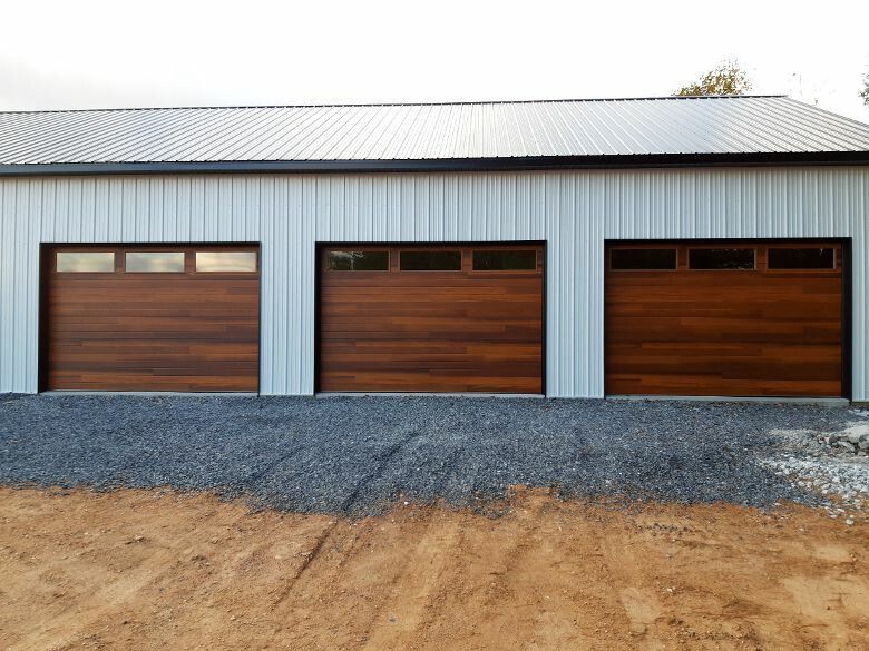 A metal garage building with three wooden doors featuring horizontal planks and small rectangular windows at the top.