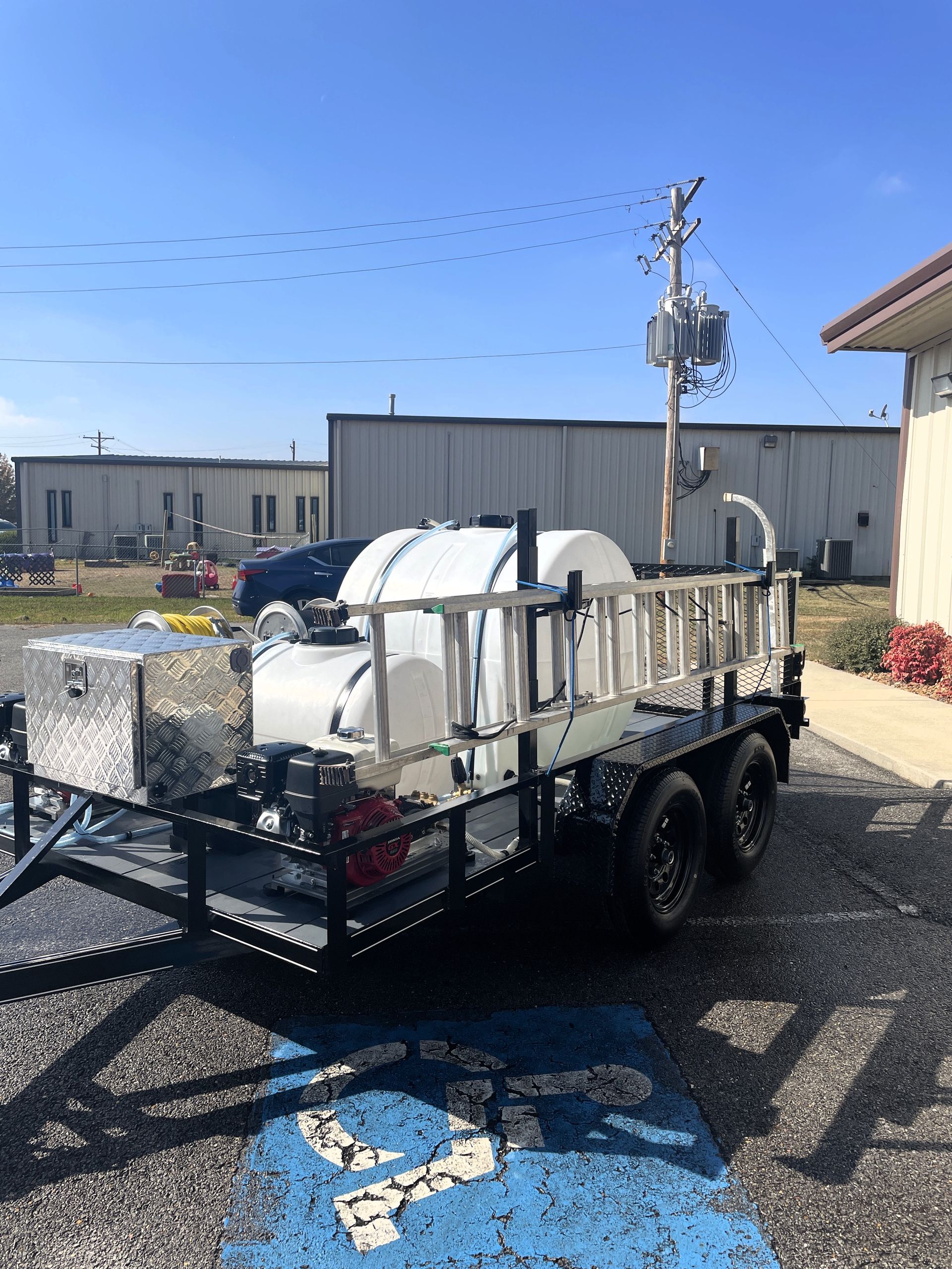 A trailer with a ladder on the back is parked in a handicapped parking spot.