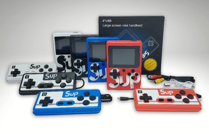 Consolas de videojuegos portátiles retro en negro, azul, rojo y blanco, dispuestas con sus embalajes detrás.
