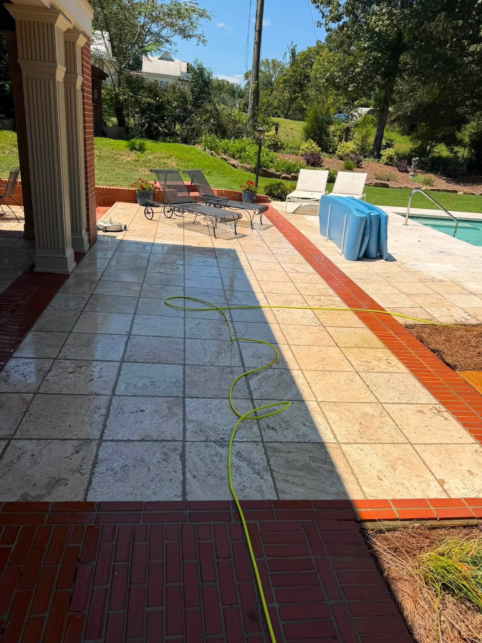 Sunny backyard patio with tiled walkway, lounge chairs, and a blue tablecloth on a table.
