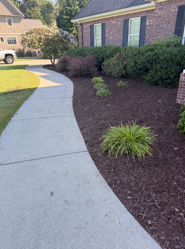 Curved concrete walkway beside a brick house with mulch beds and shrubs