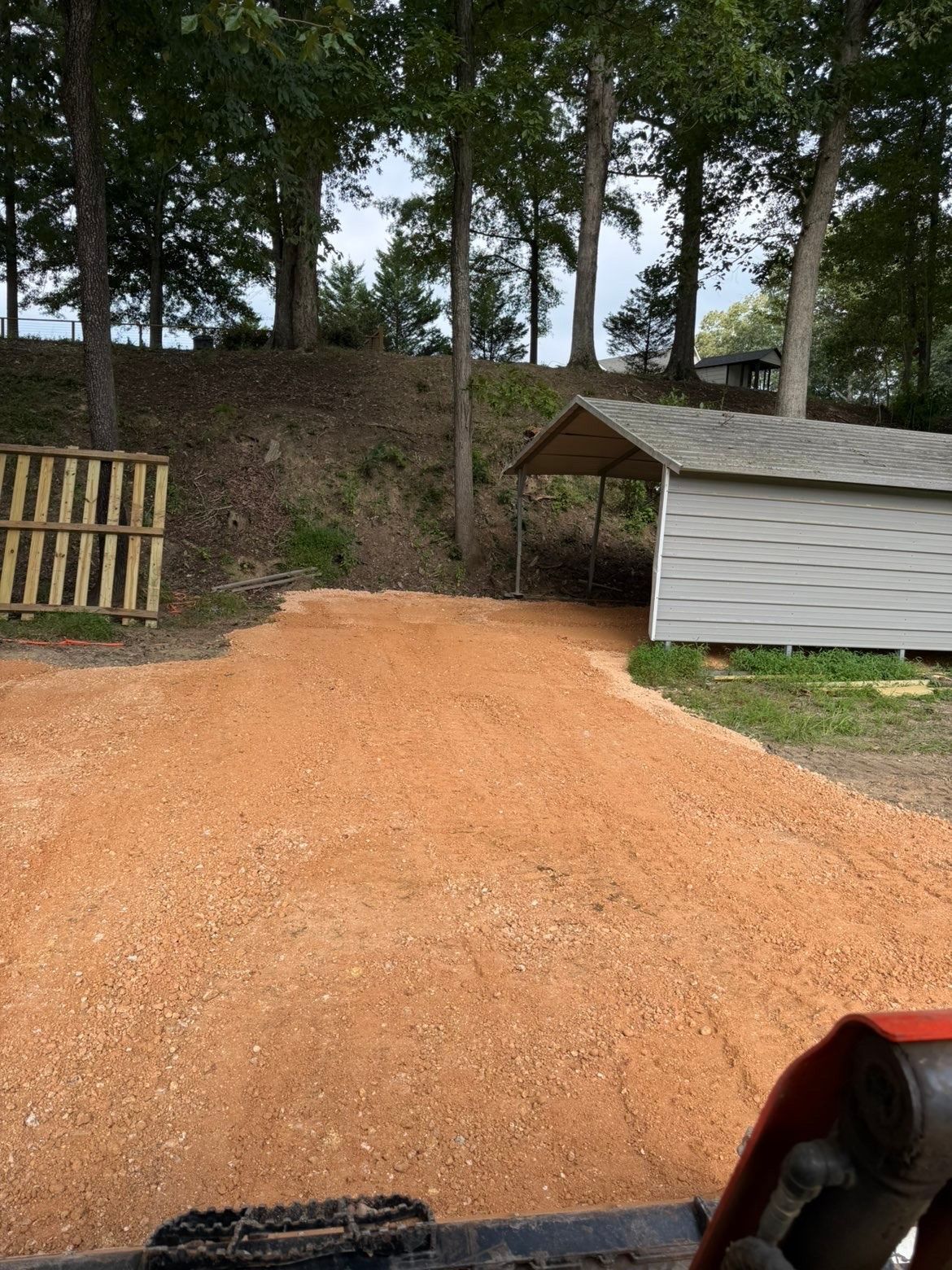 Gravel driveway leading to a shed and trees on a wooded hillside.