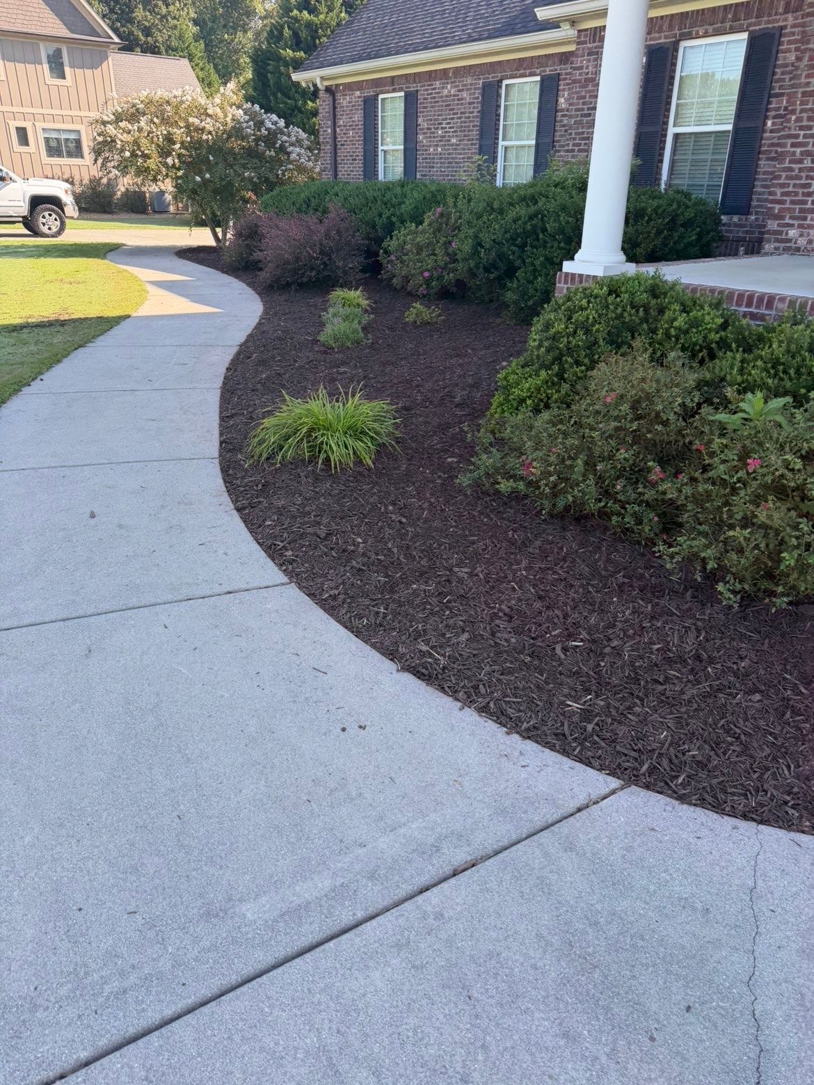 Curved concrete walkway beside brick house and landscaped shrubs with mulch