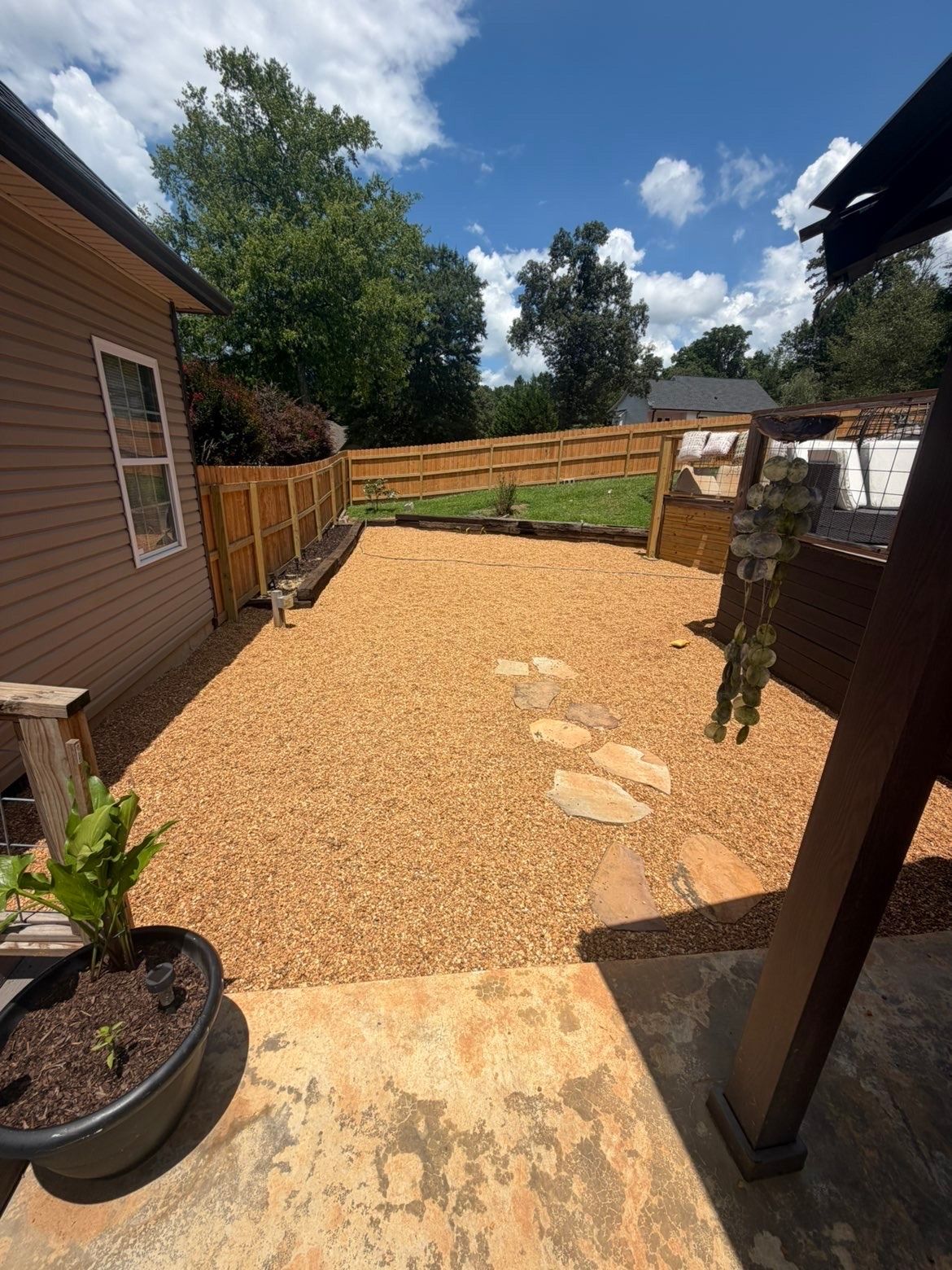 Gravel backyard with wooden fence, stepping stones, potted plant, and patio under a blue sky