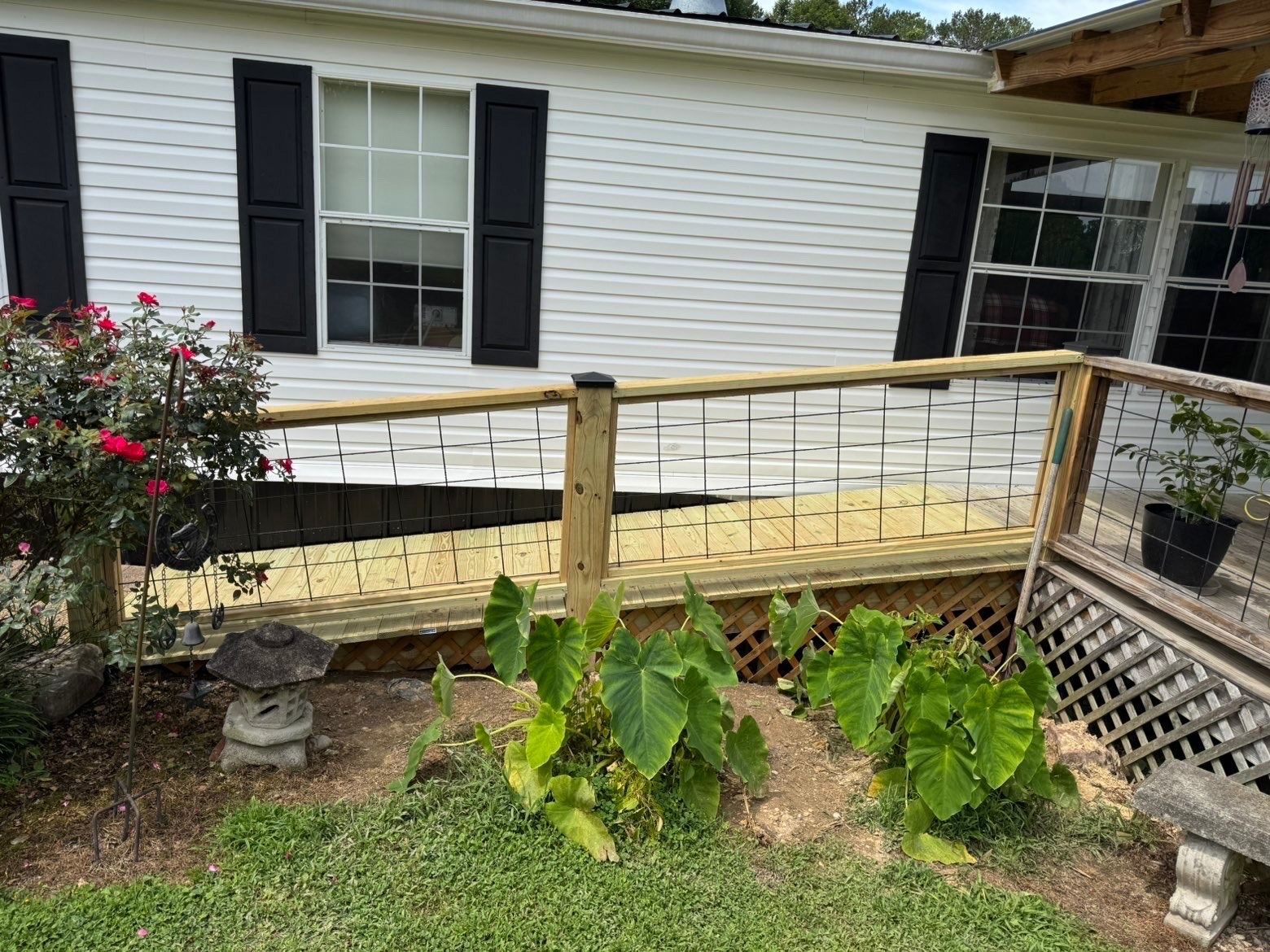 Wooden wheelchair ramp with railings beside a white house with black shutters and steps.