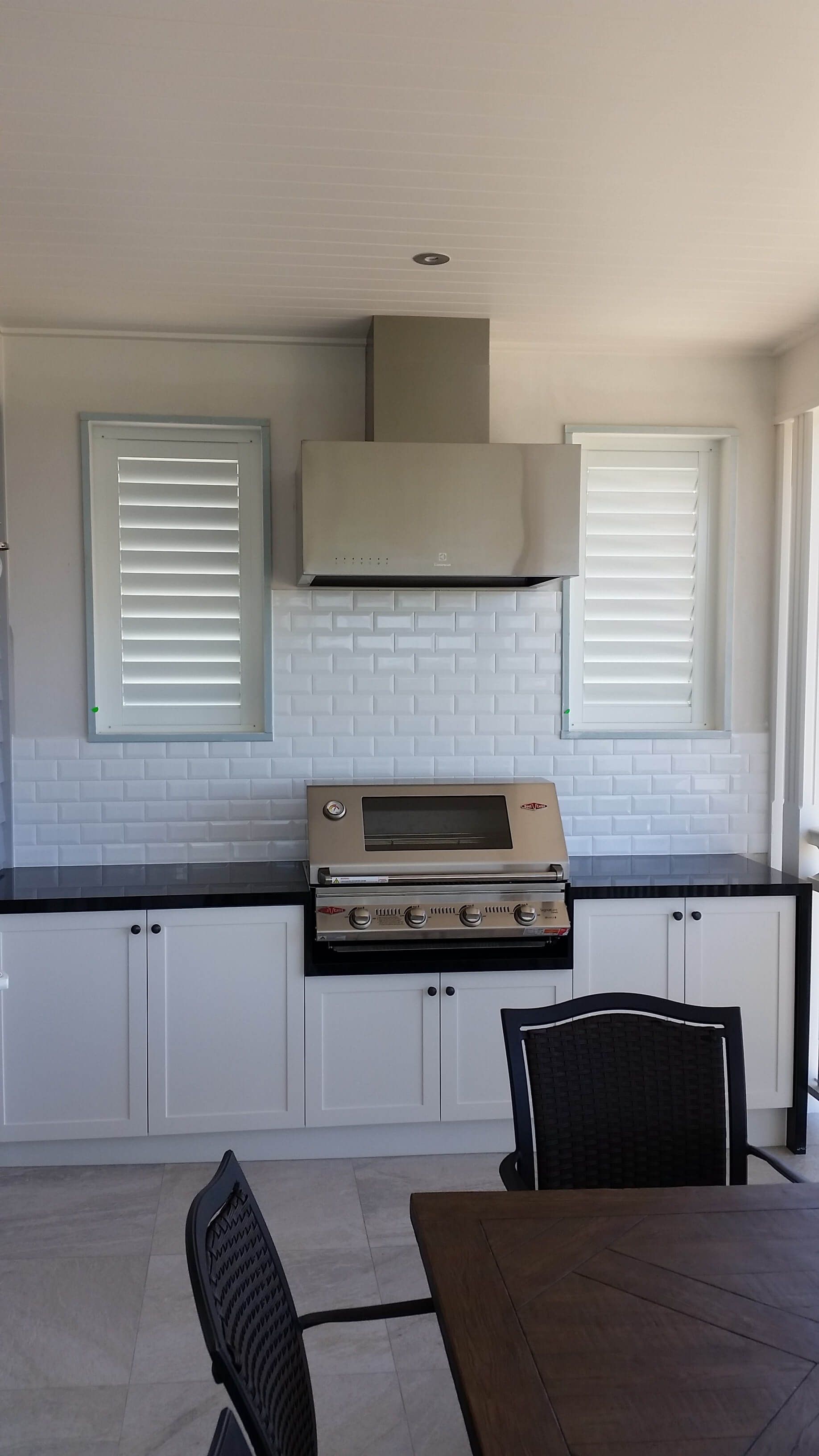 Modern kitchen with white cabinets, black countertops, stove, hood, and louvered window shutters.