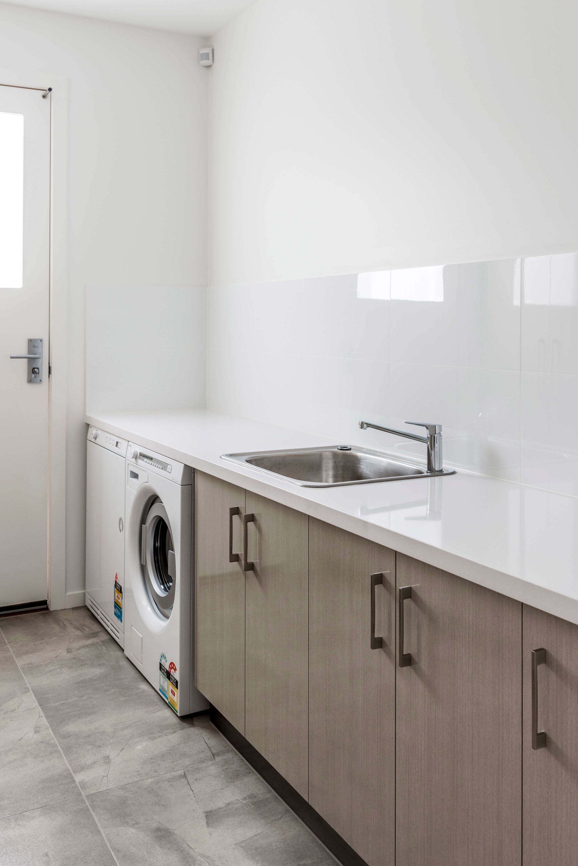 Modern laundry room with sink, front-loading washer, and wood cabinets along a white countertop.