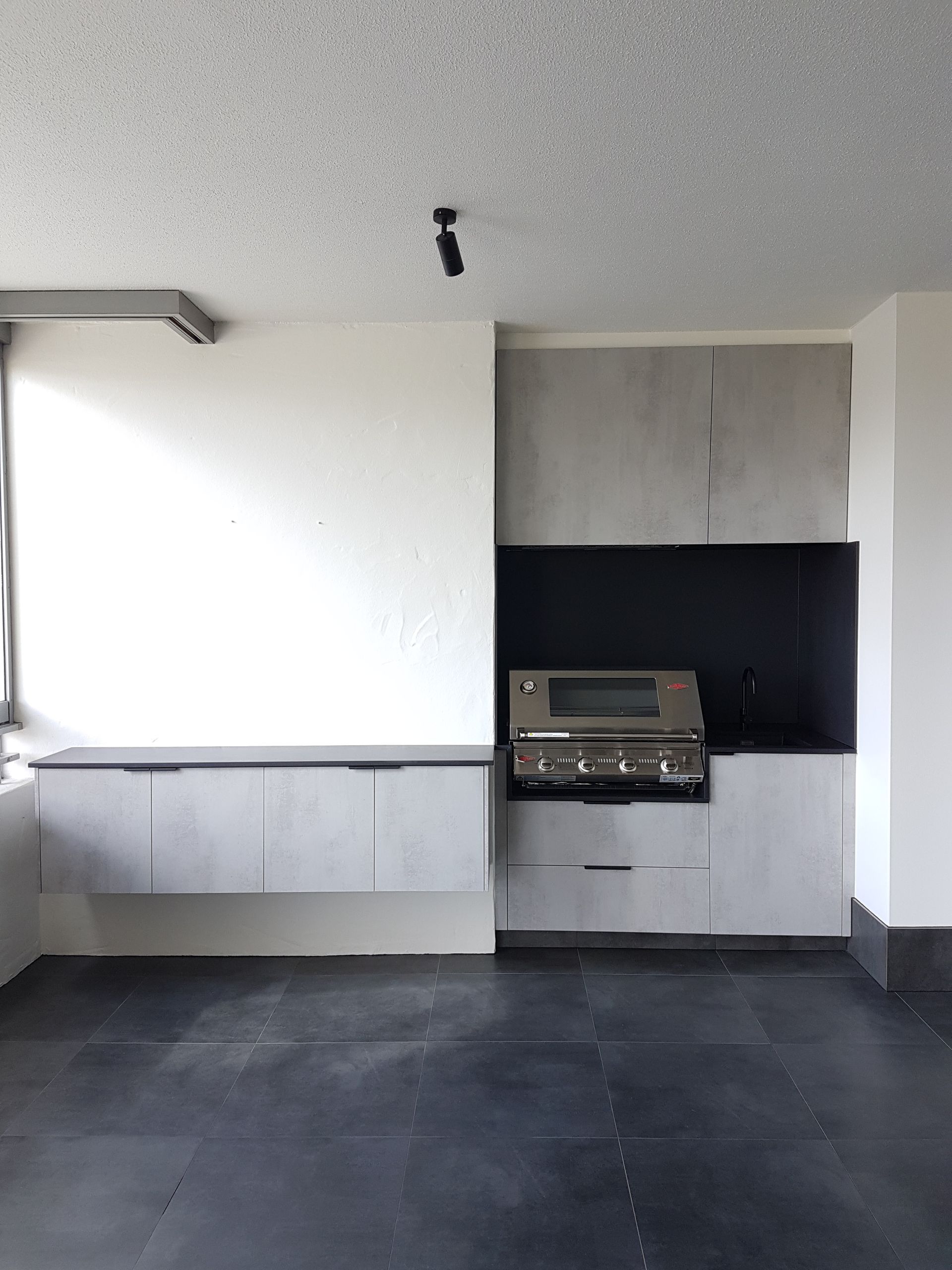 Empty modern interior with built-in cabinets, a sink counter, and a small built-in grill on a dark floor.