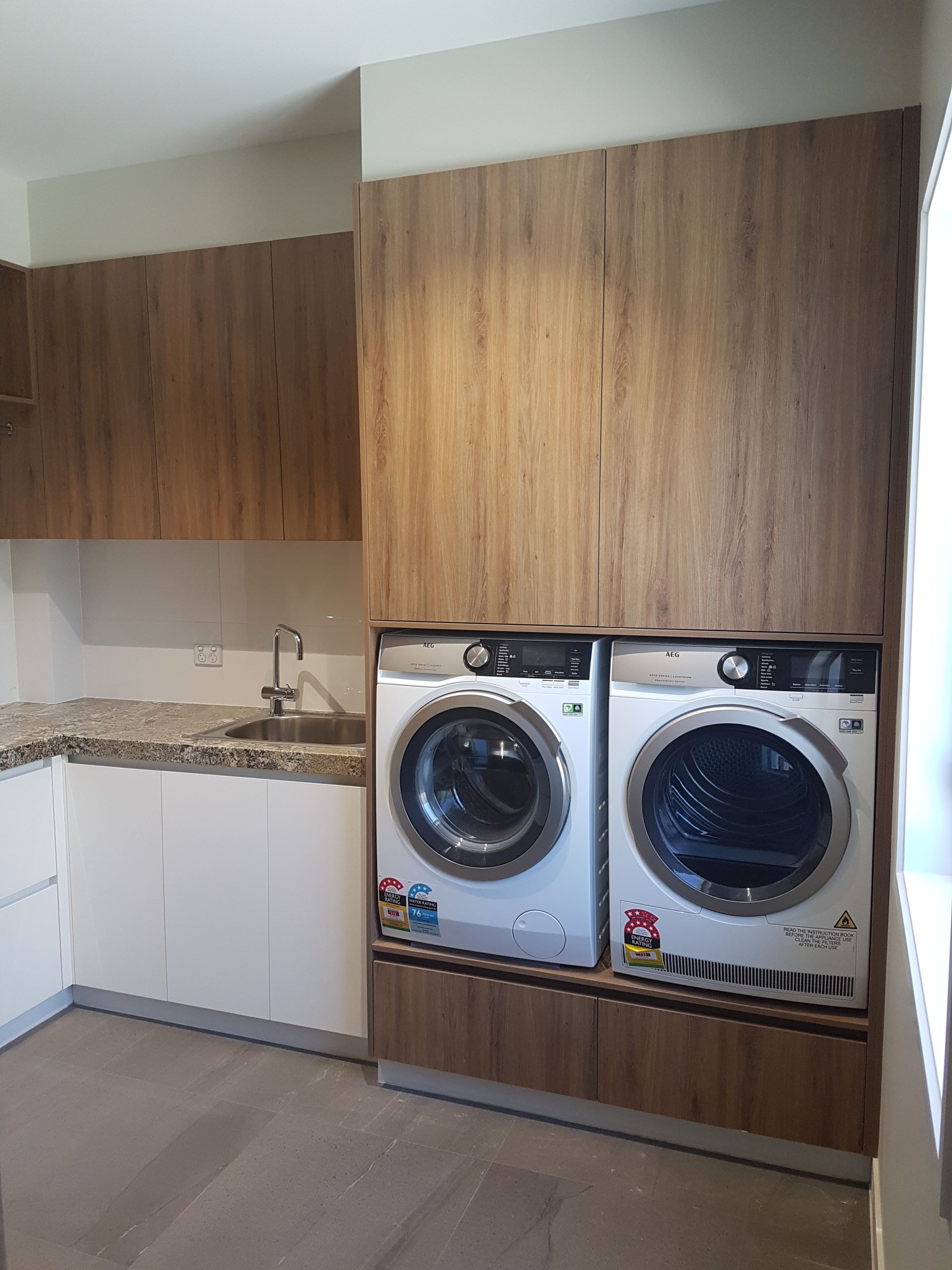 Small laundry room with white cabinets, wood panels, a sink, and stacked washer-dryers.