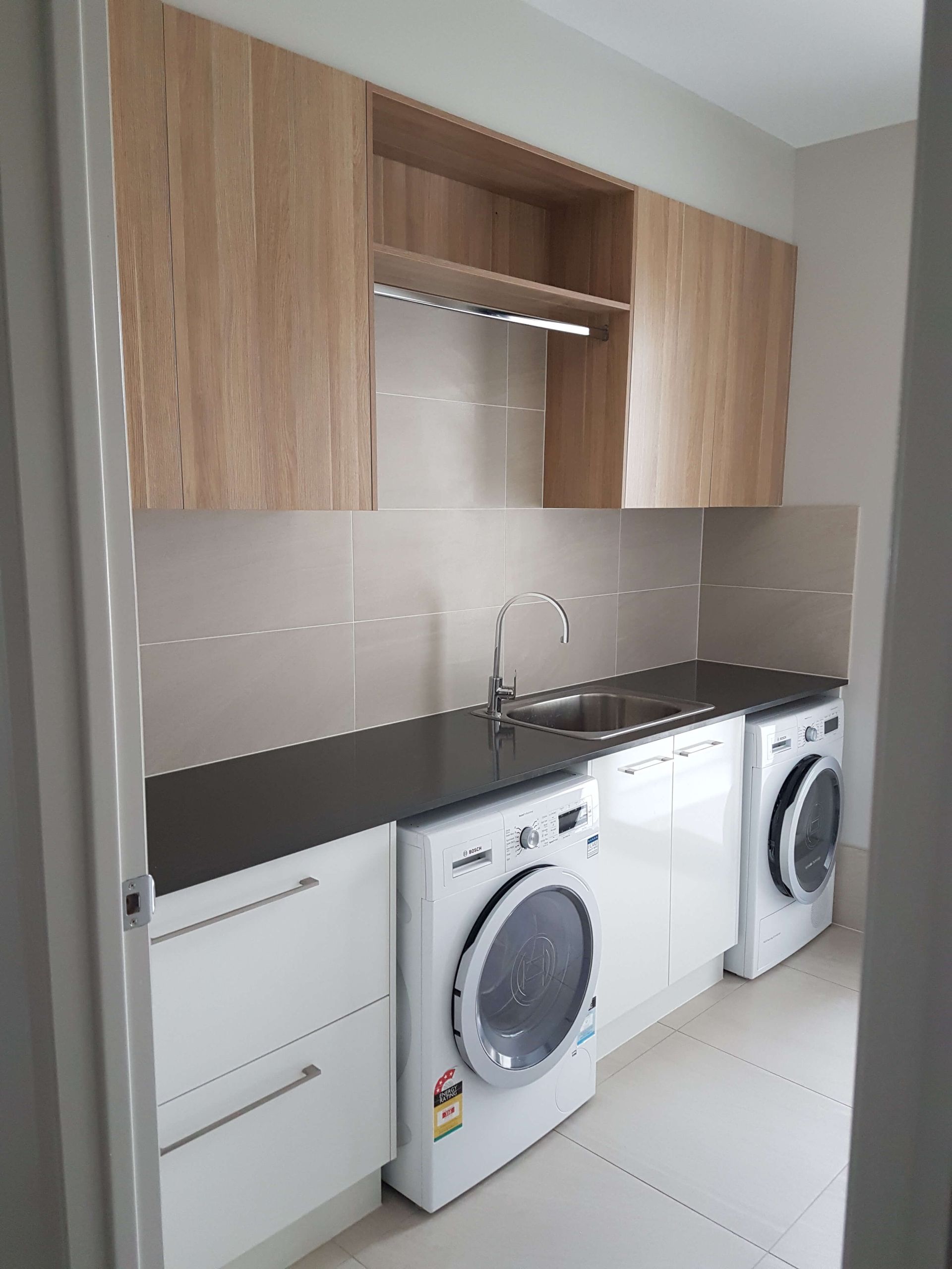 Compact laundry room with wood cabinets, sink, countertop, and two front-loading appliances.