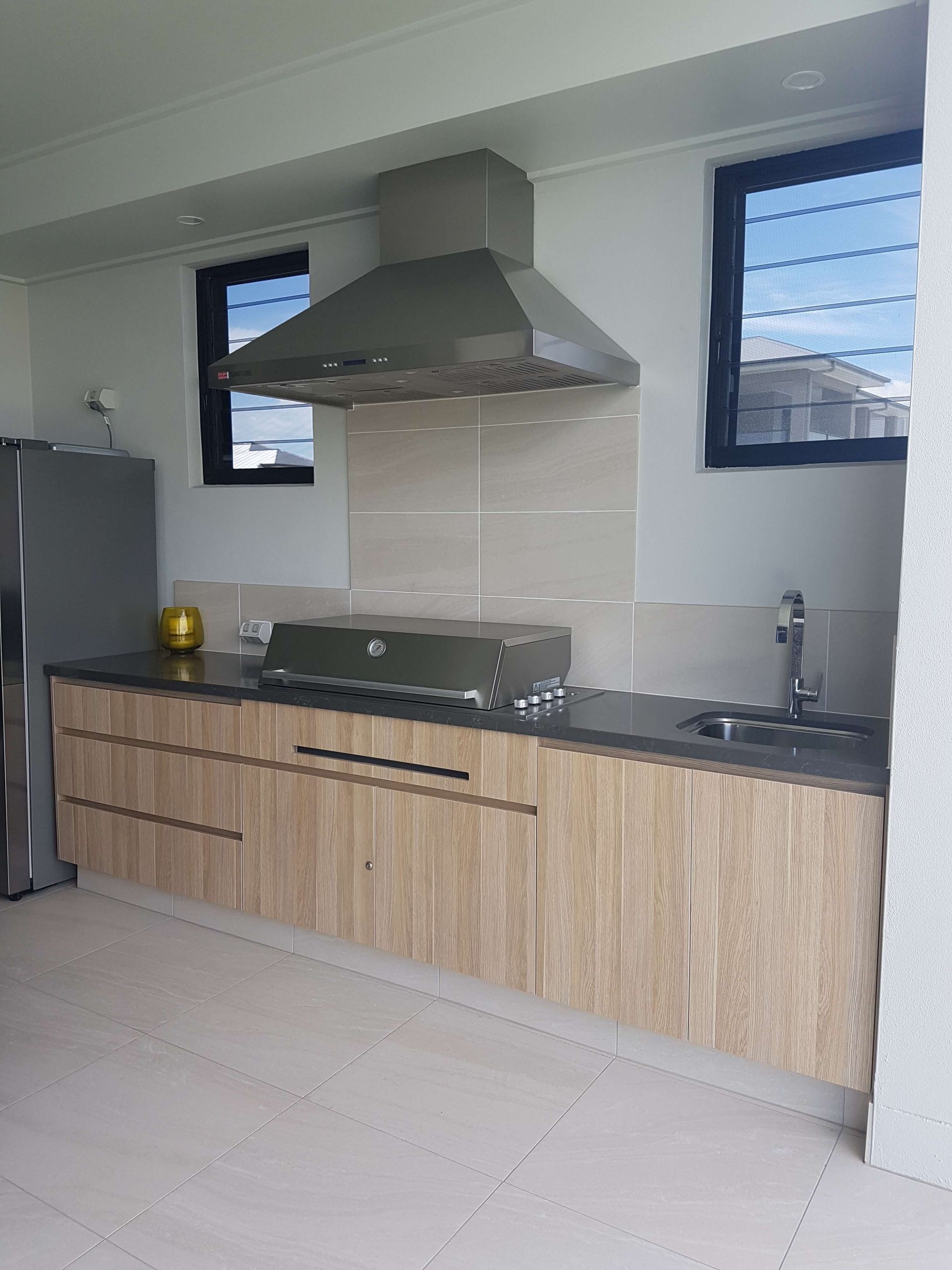 Modern kitchen with wood cabinets, gray countertop, stainless range hood, and two narrow windows.