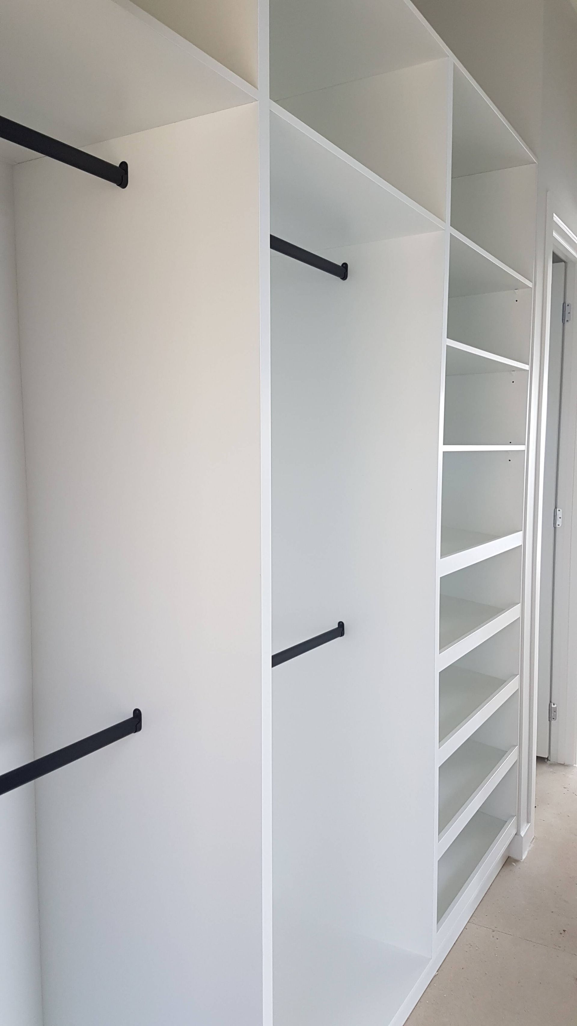 White built-in closet shelving and hanging rods in a bright hallway or bedroom closet area