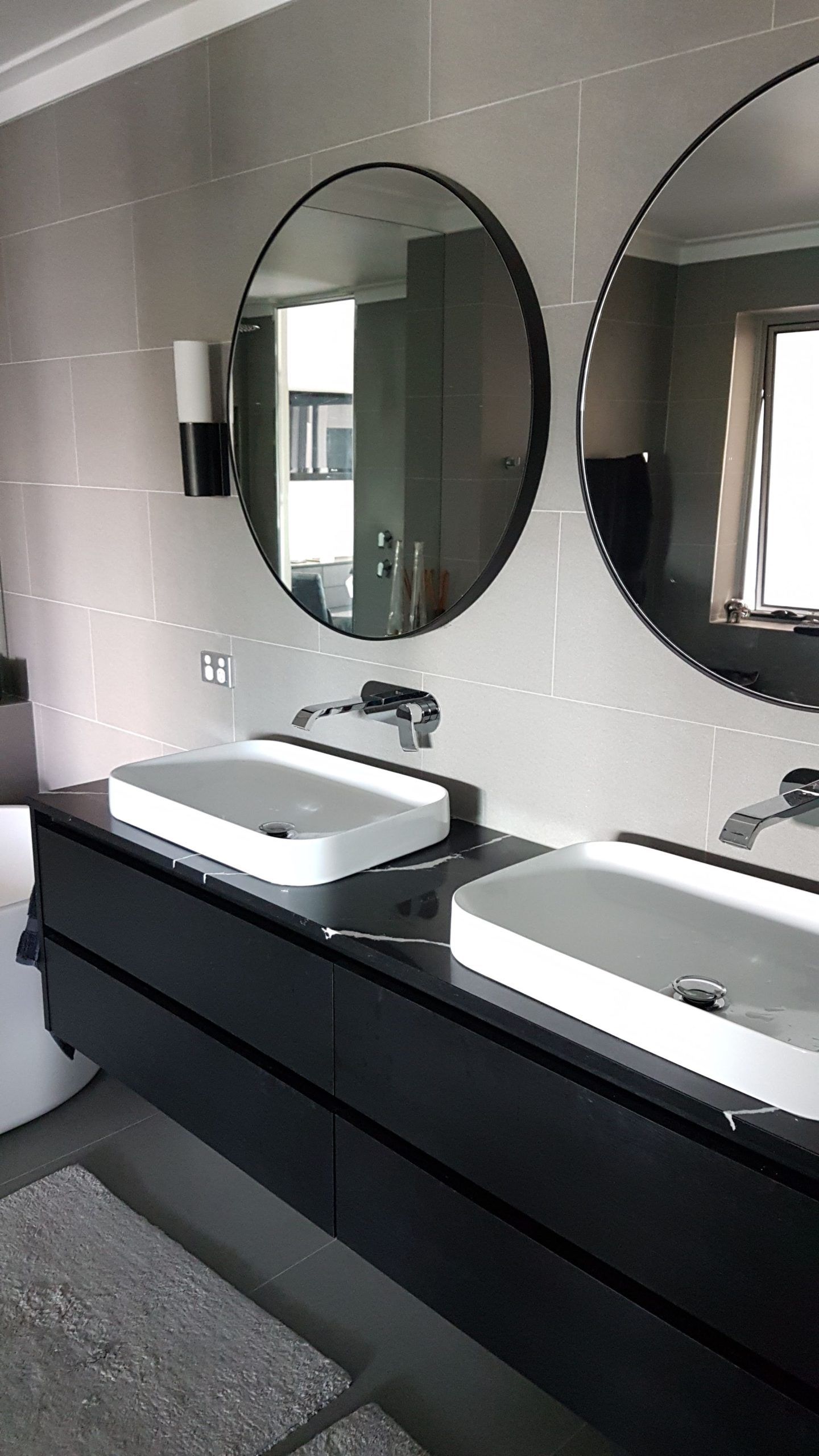 Modern bathroom vanity with two sinks, round mirrors, and dark cabinets beside a gray wall.