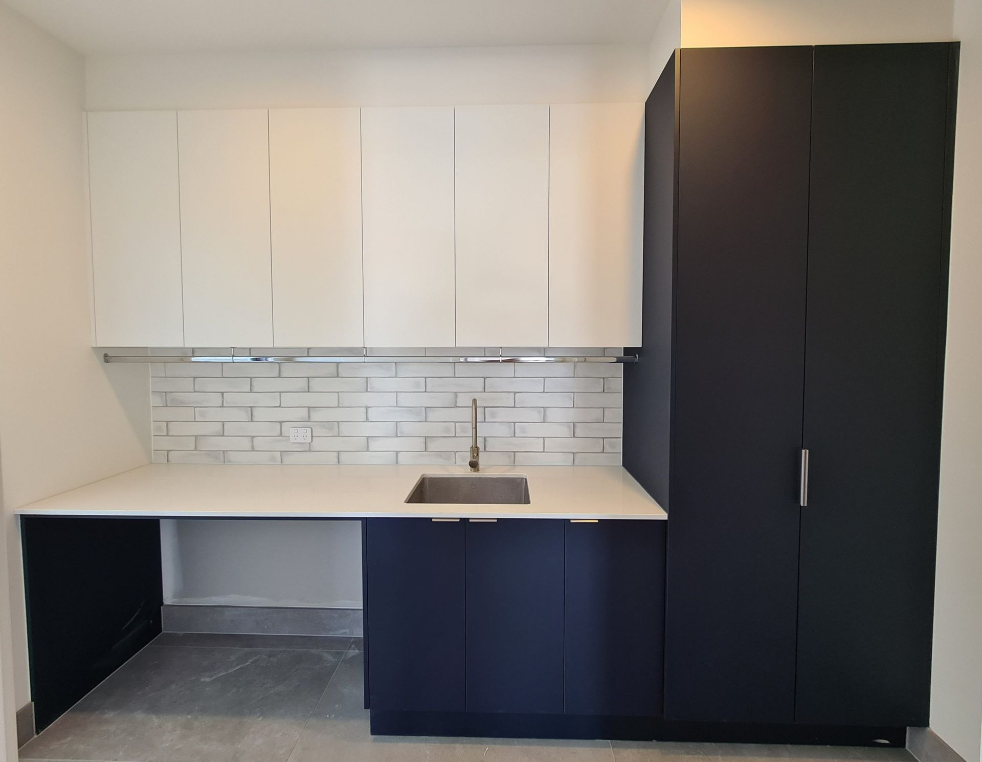 Modern kitchen with white upper cabinets, dark lower cabinets, white tile backsplash, and a built-in desk nook