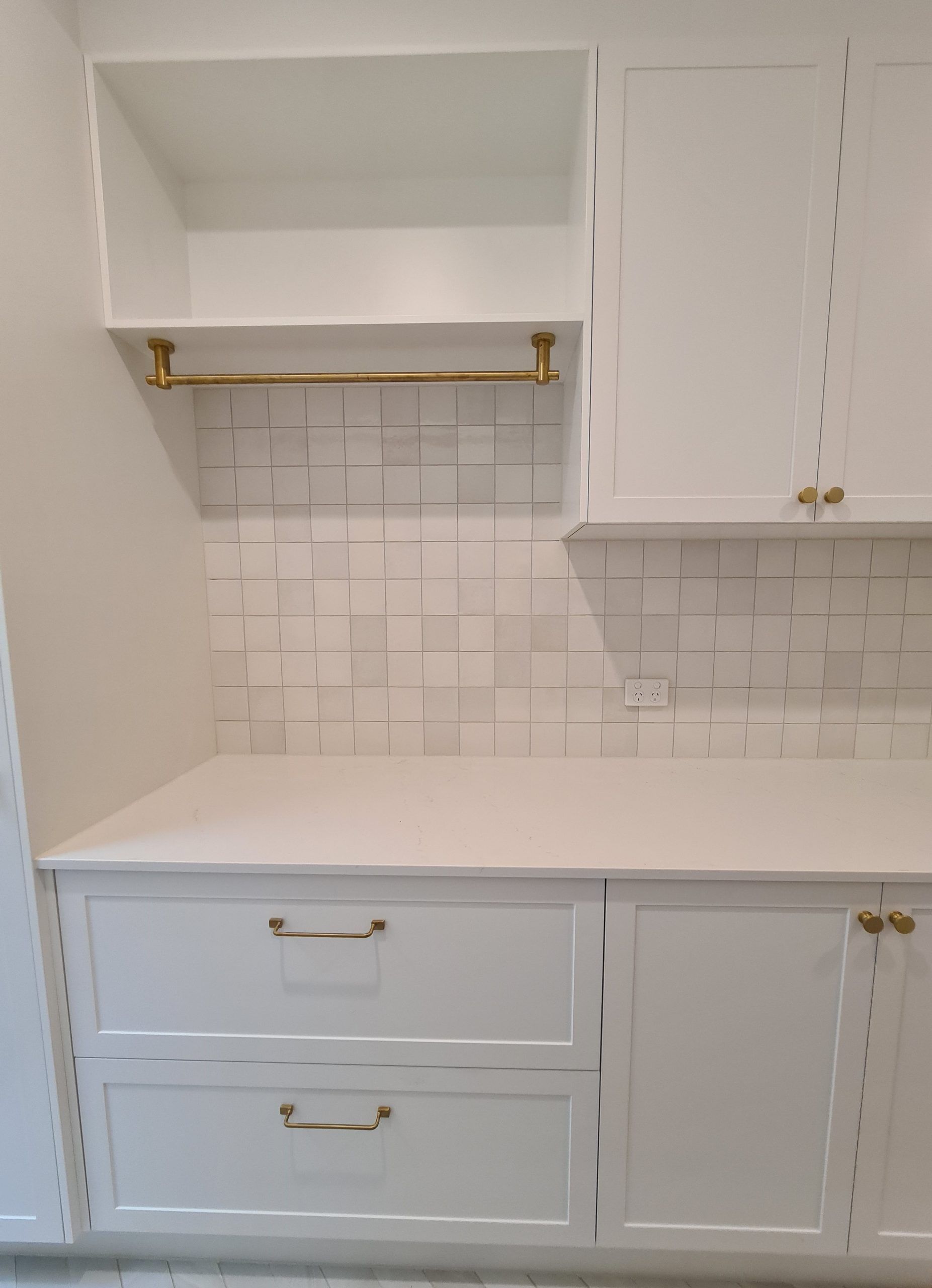 White kitchen cabinetry with open shelf, brass rail, white subway tile backsplash, and white countertop.