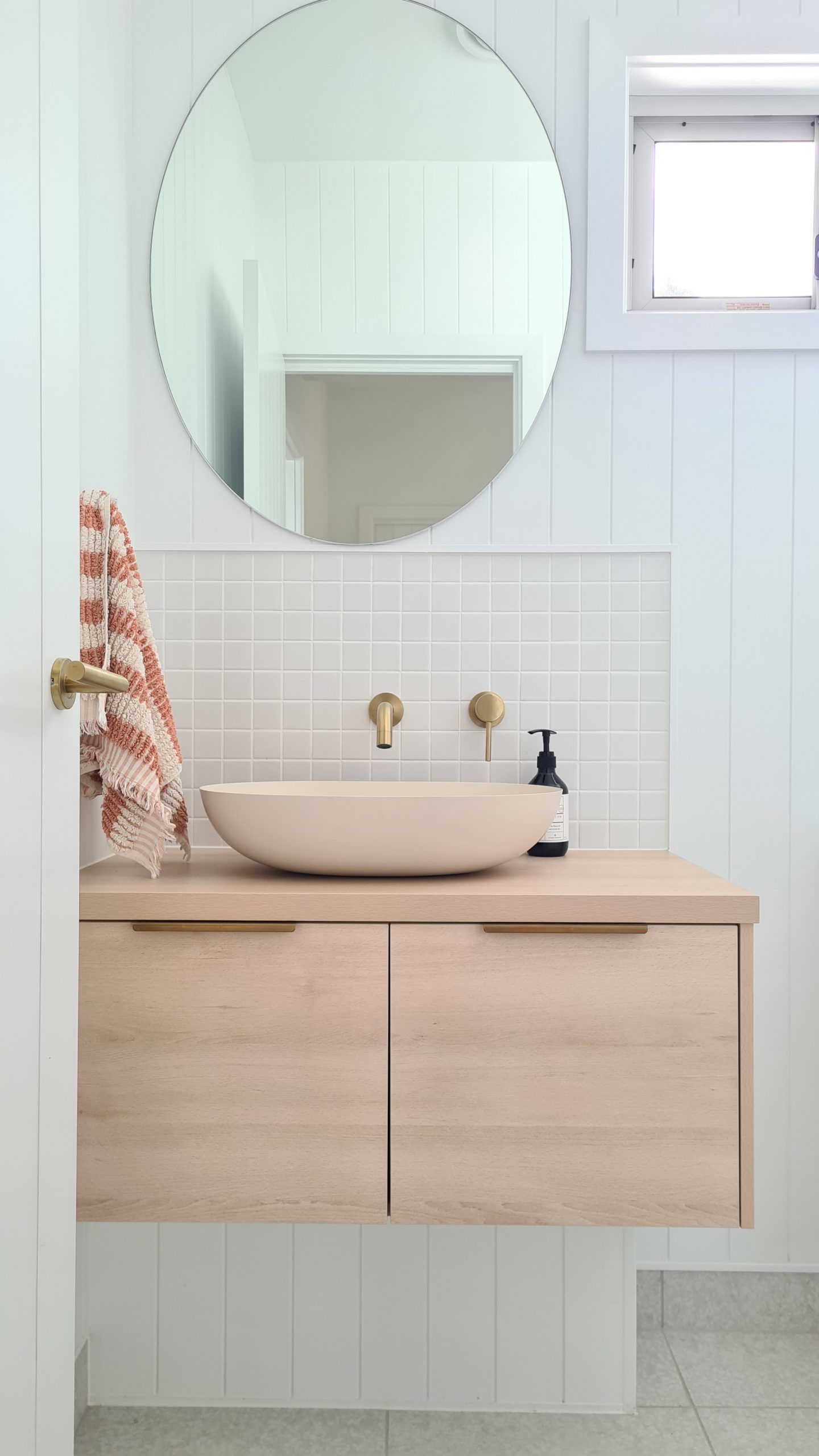 Minimal bathroom vanity with round mirror, white vessel sink, and light wood cabinets.