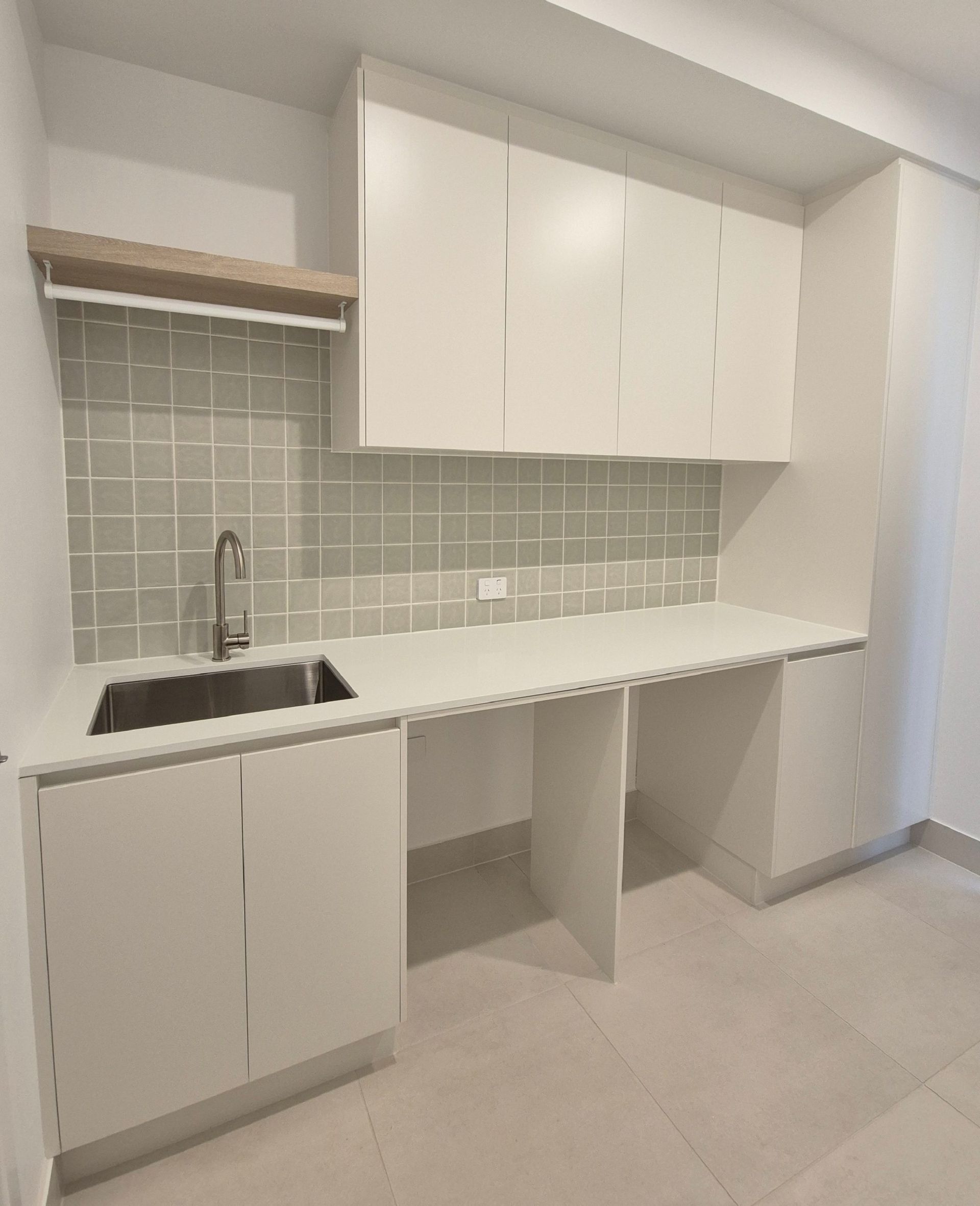 Compact white kitchenette with sink, cabinets, gray tile backsplash, and open shelving in a small room