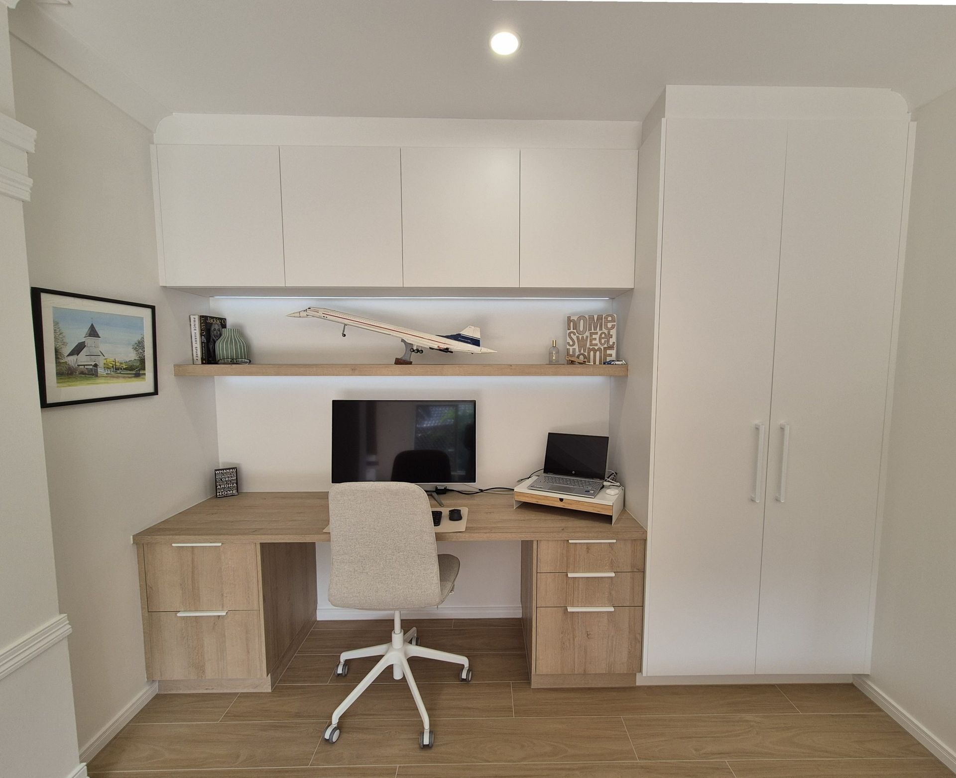 Modern home office with white desk, chair, built-in cabinets, and computer monitor in a bright room.