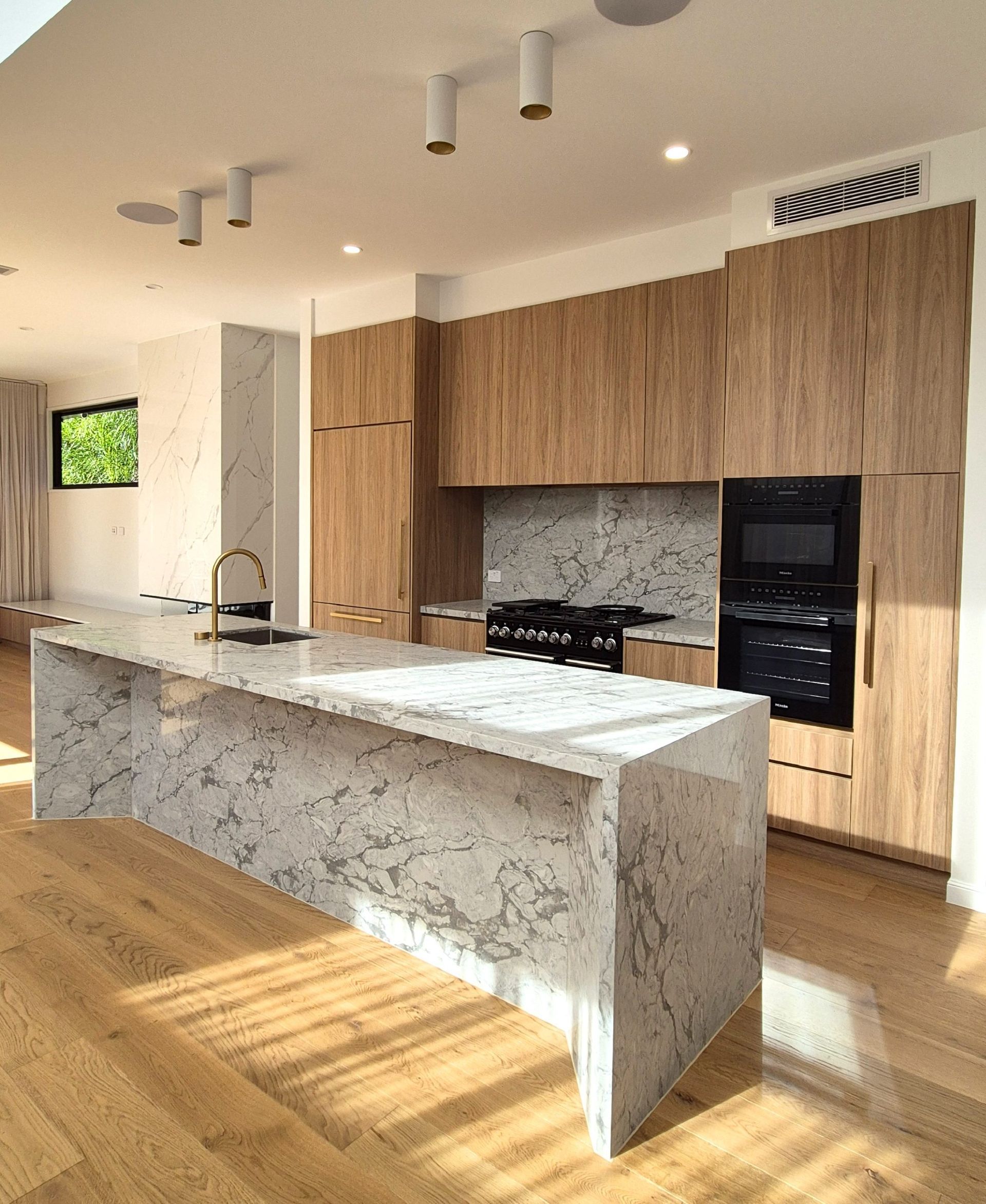 Modern kitchen with wood cabinets, marble island, black appliances, and sunlit hardwood floors. Modern kitchen with wood cabinets, marble island, black appliances, and sunlit hardwood floors.