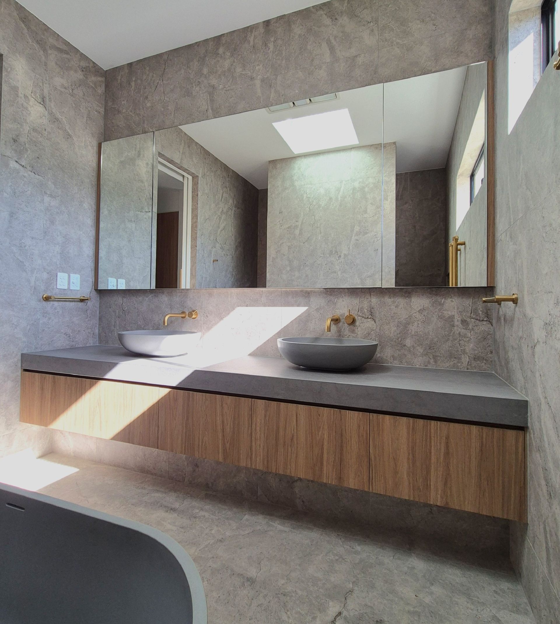 Modern bathroom with concrete walls, floating wood vanity, vessel sink, mirror, and skylight lighting