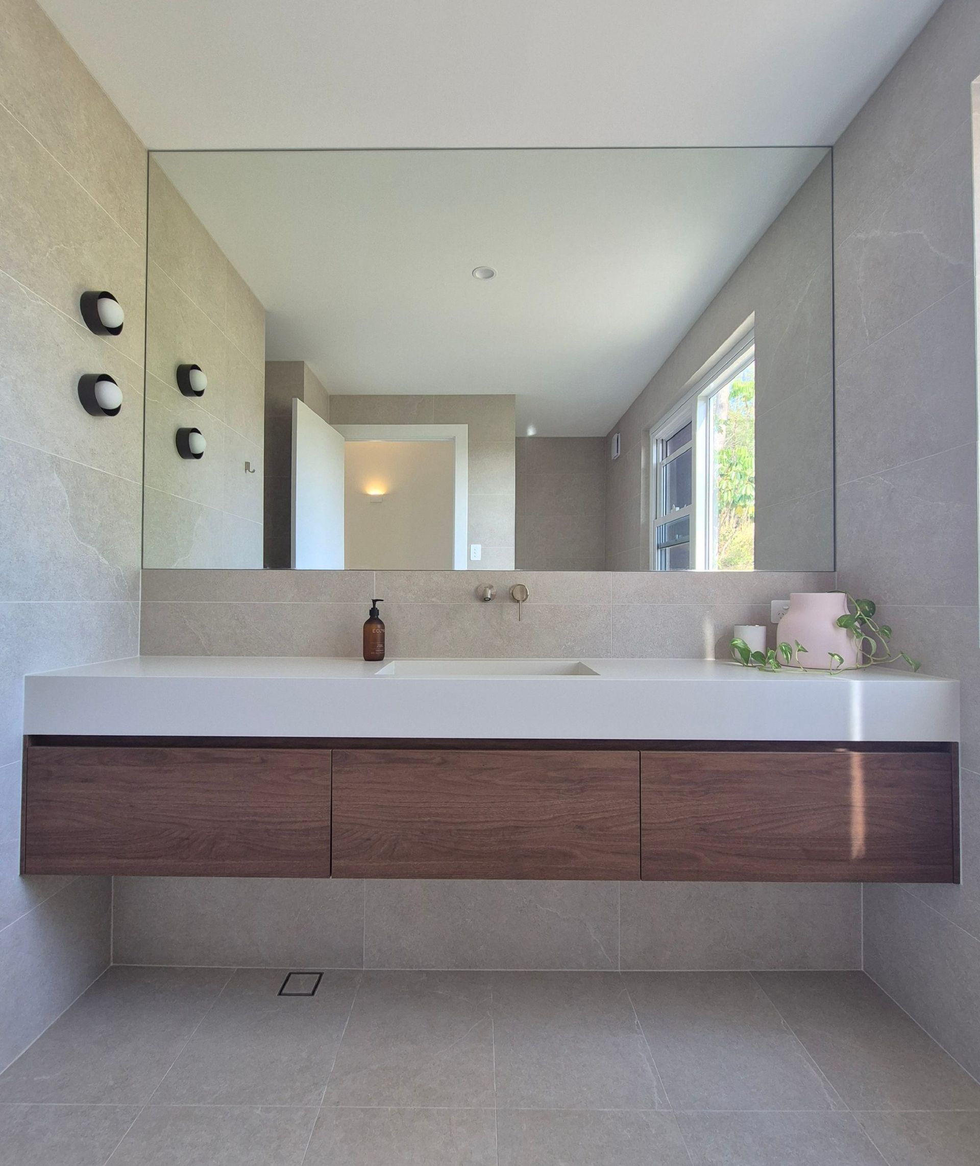 Modern bathroom with floating wood vanity, large mirror, and white sink beside a window.