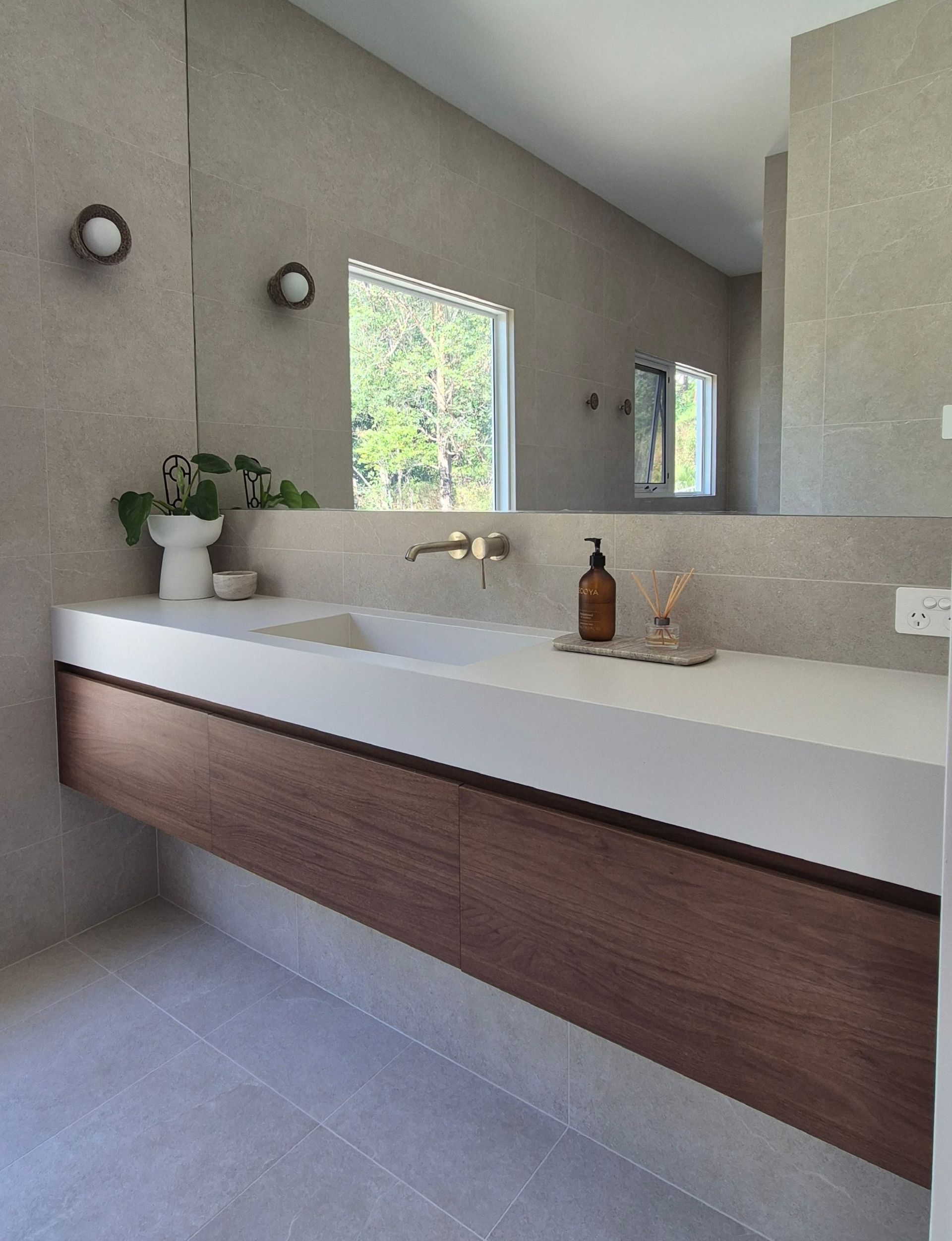 Modern bathroom vanity with floating wood cabinet, white sink, mirror, and large window.