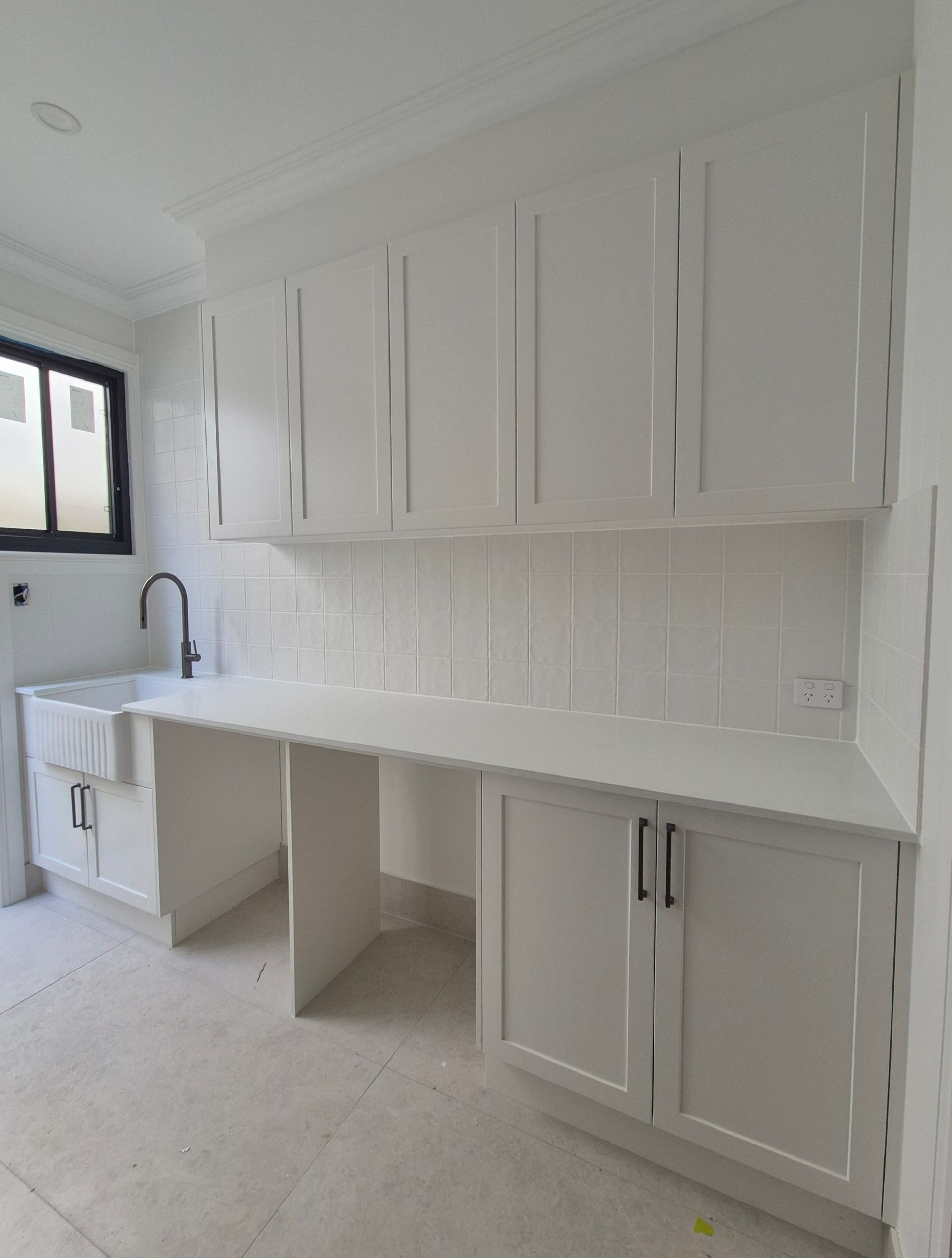 White kitchen with shaker cabinets, white countertops, and a sink by a window.