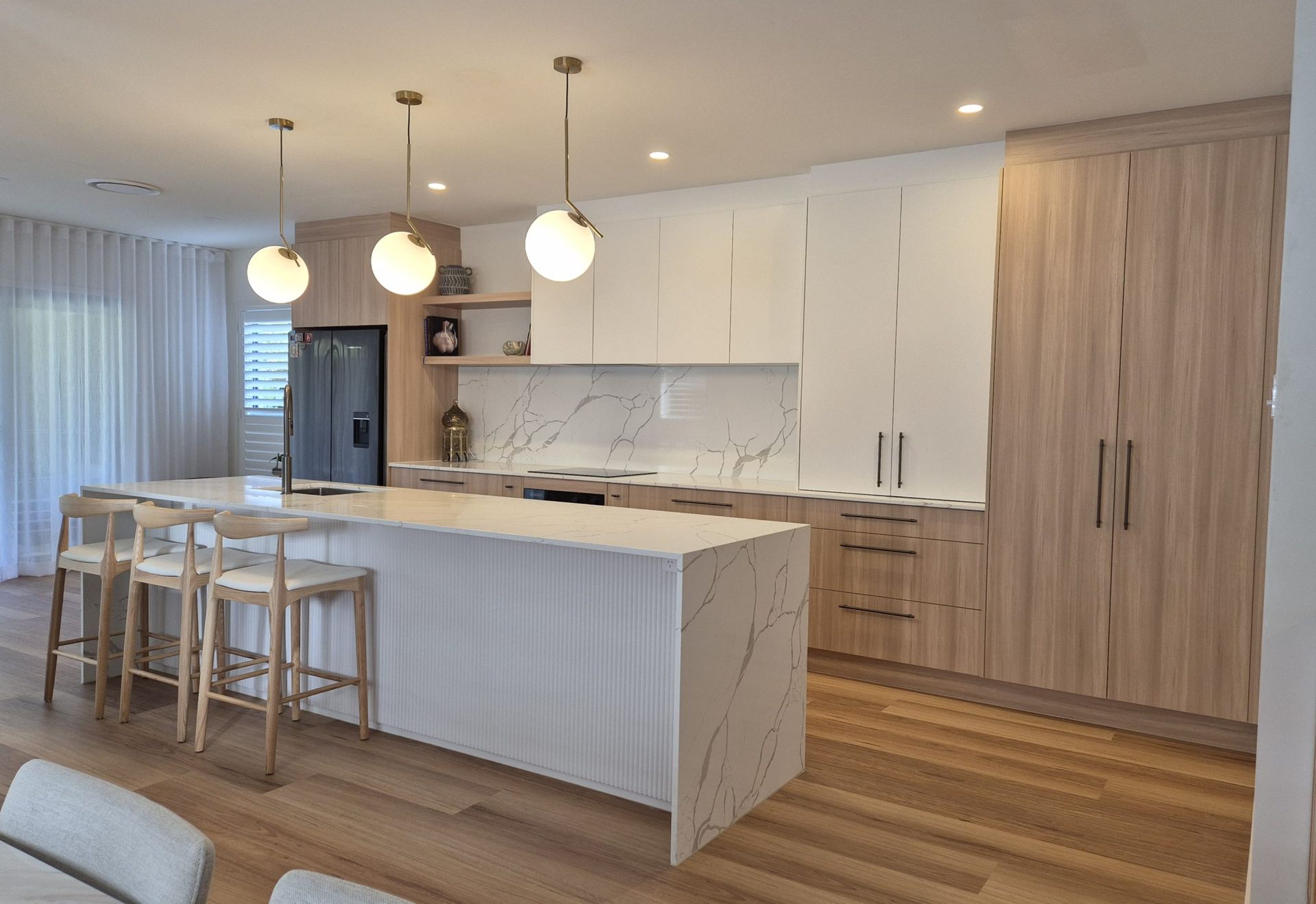 Bright modern kitchen with white island, wood floors, pendant lights, and bar stools Bright modern kitchen with white island, wood floors, pendant lights, and bar stools