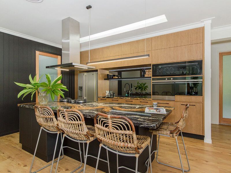 Modern kitchen with wood cabinets, island barstools, stainless steel appliances, and a plant on the counter
