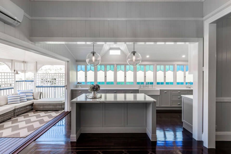 Bright white kitchen with central island, dark wood floors, and sunlit windows over the sink Bright white kitchen with central island, dark wood floors, and sunlit windows over the sink