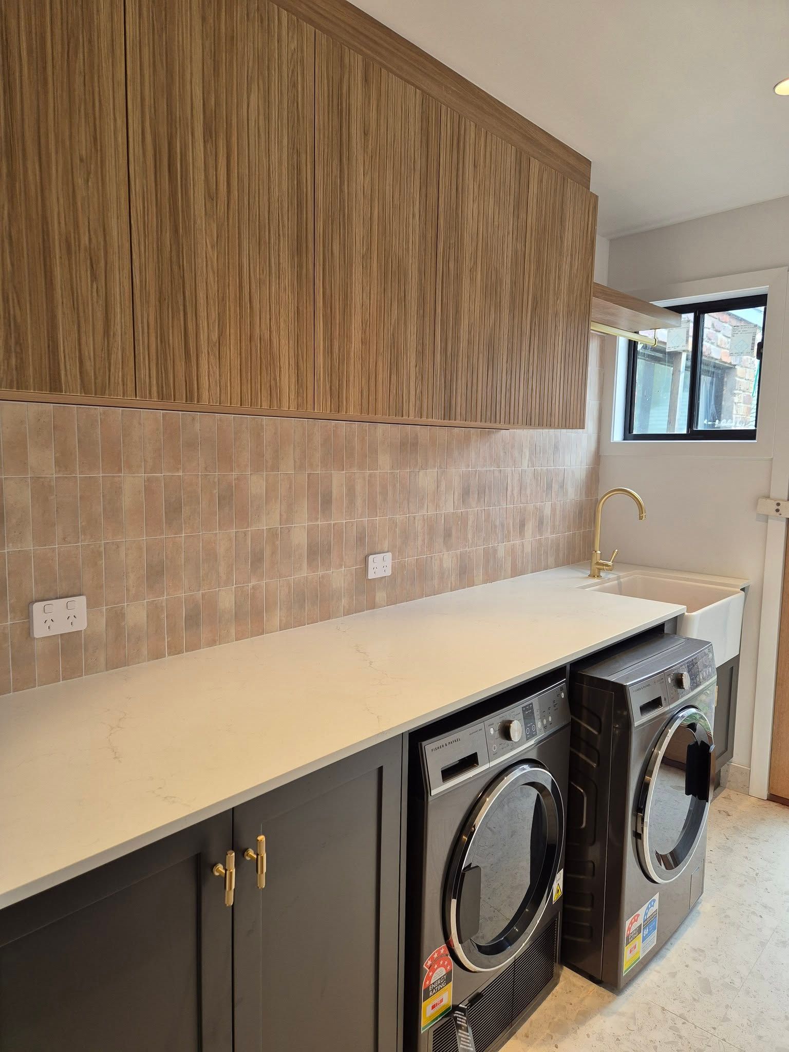 Modern laundry room with stacked washer-dryer, beige countertop, dark cabinets, and tan tile backsplash